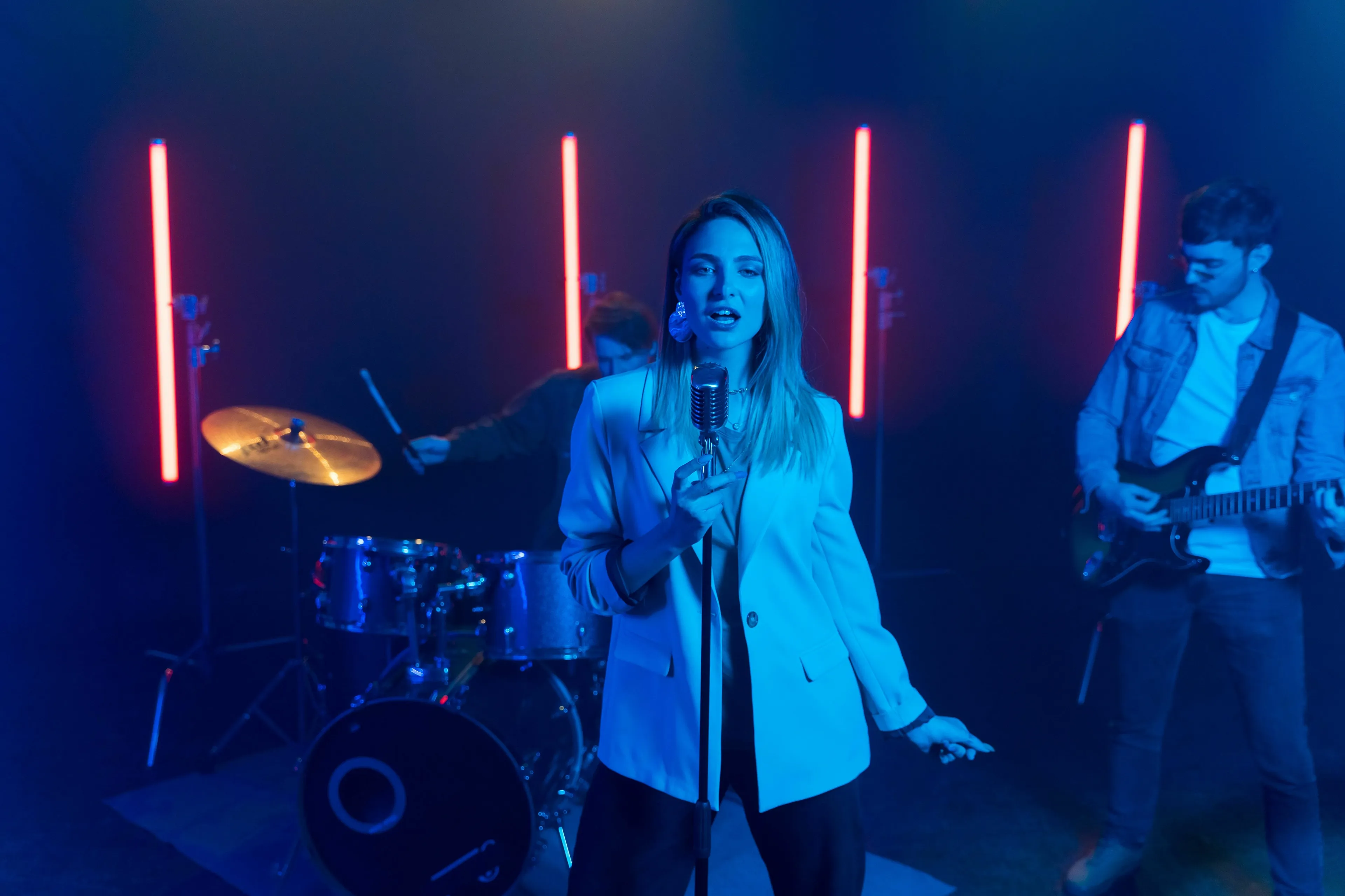 Music quiz: A band performs live, with the female singer holding a vintage microphone under neon lights.