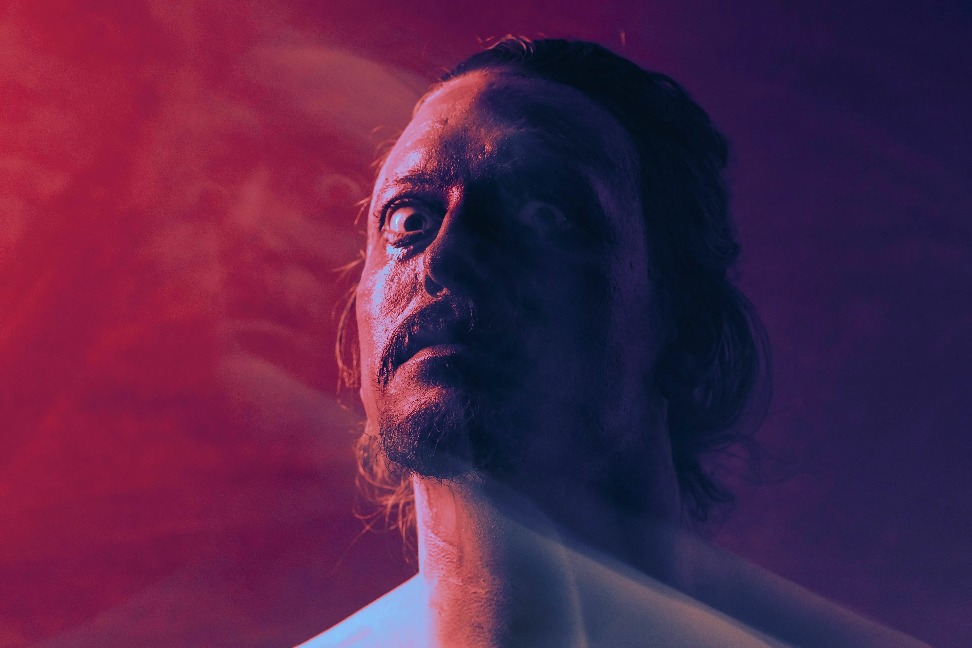 Music quiz: A man with an intense gaze, illuminated by red and blue light, suitable for a quiz about a singer known as The Prince of Darkness.