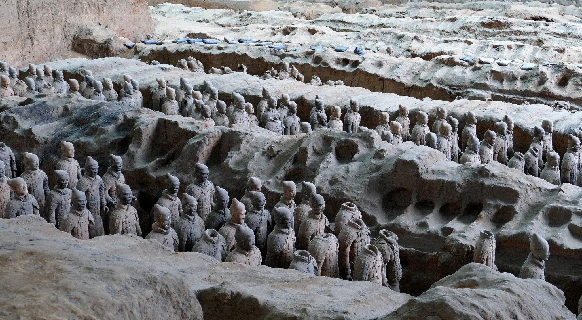 Rows of Ancient Civilizations Terracotta Army figures, some partially unearthed from the dirt, standing guard.