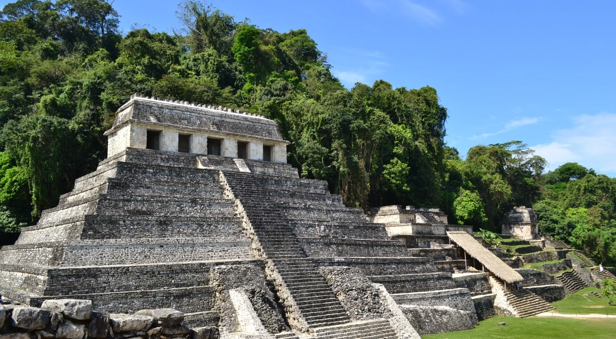 The ancient city of Palenque with its stone Mayan temples and pyramids nestled in lush jungle under a clear blue sky.