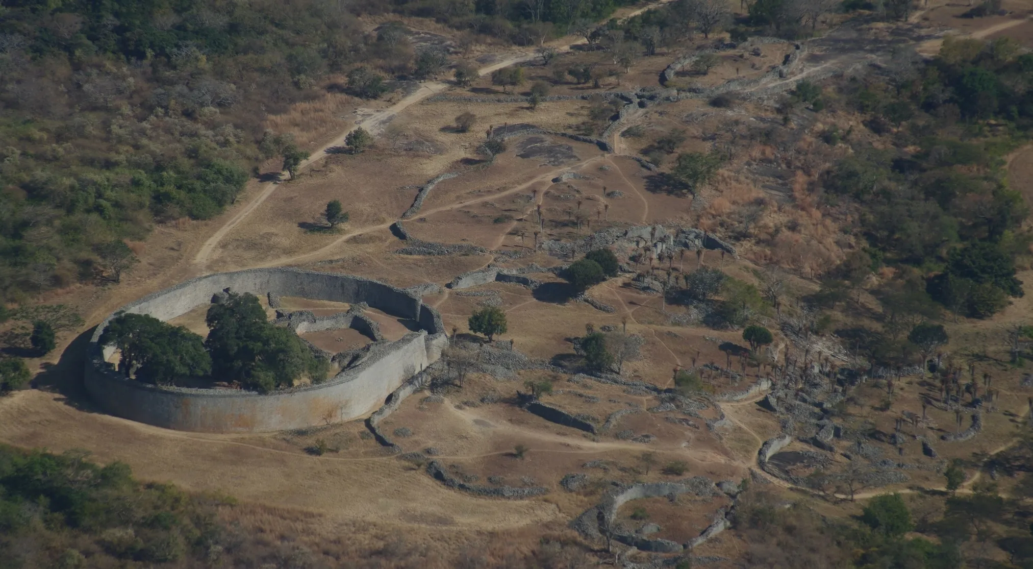 Aerial view of the Great Zimbabwe ancient civilization, showing its massive stone structures amidst dry landscape and trees.