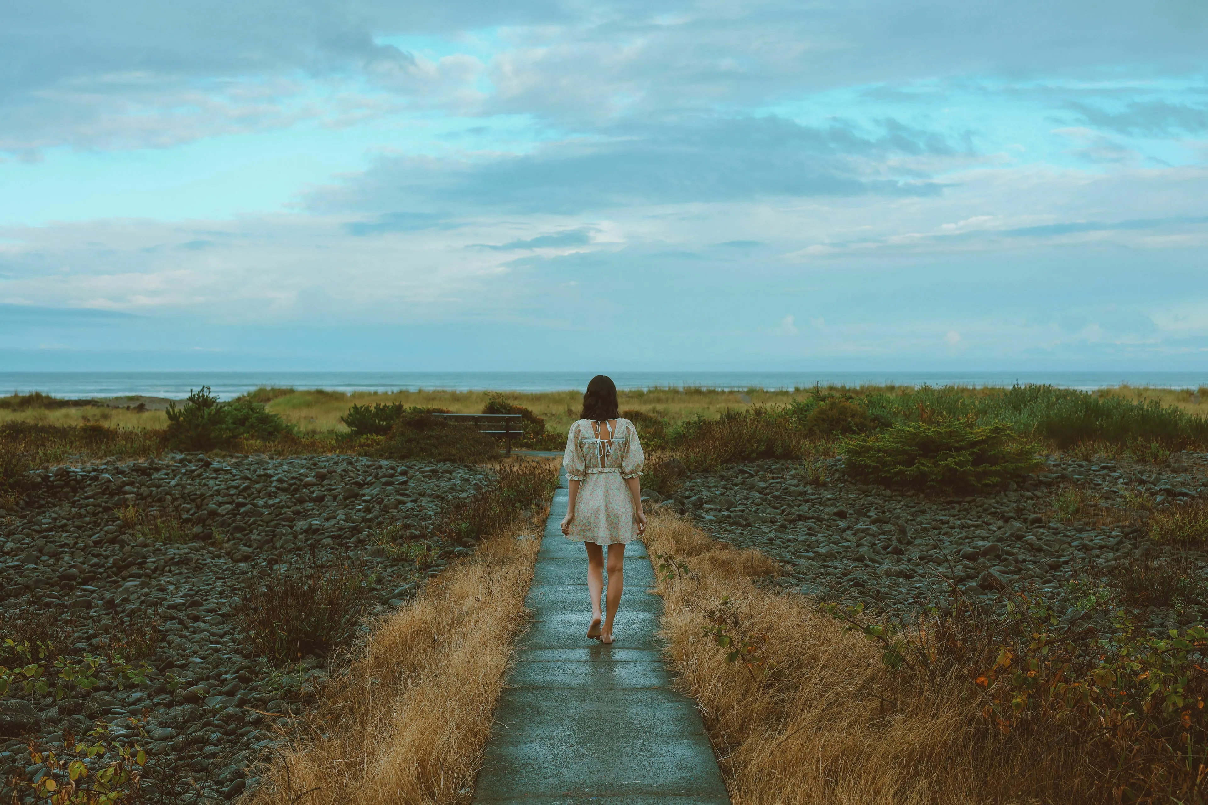 A woman walks a path towards the sea, contemplating a mythological quest requiring her to leave someone behind.