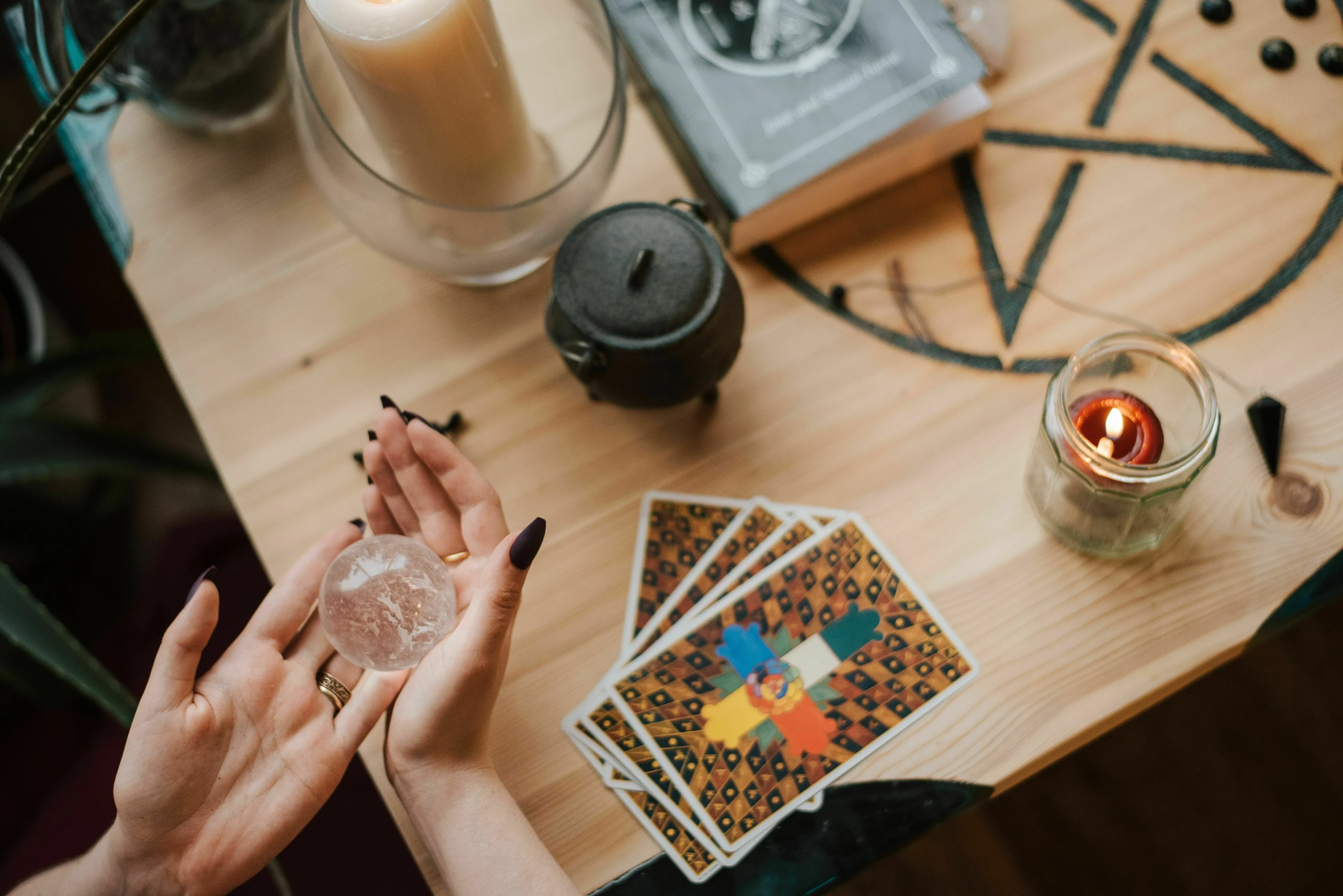 Hands holding a crystal ball beside tarot cards, candles, and a pentagram, hinting at a prophecy for a mythological quest.