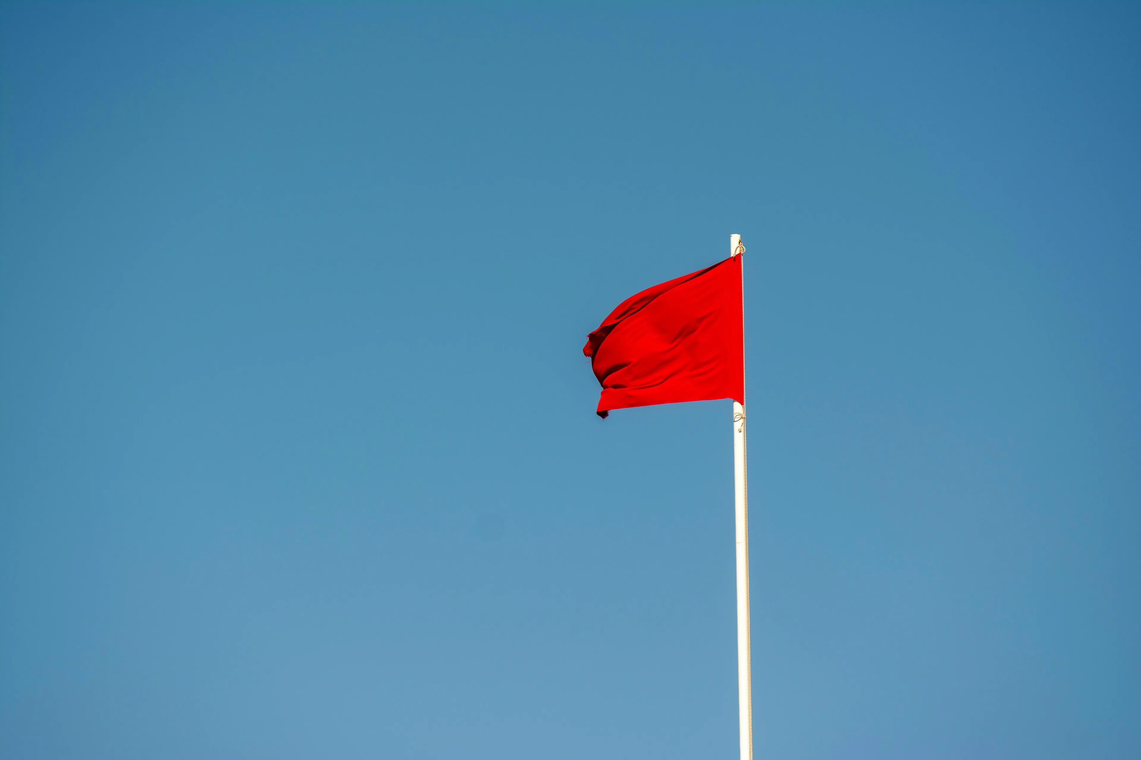 A red flag waving against a clear blue sky.