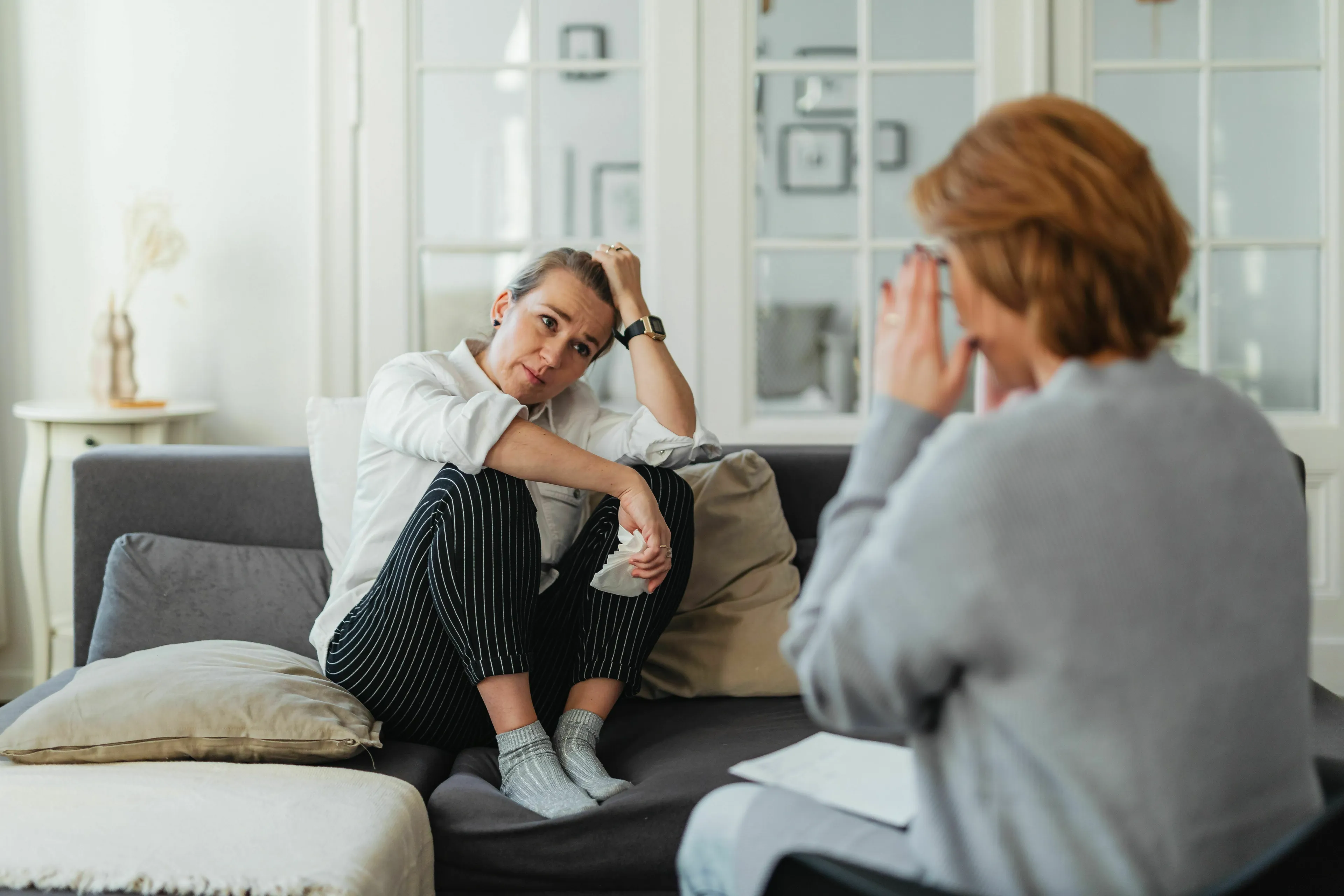 Green Flag: A woman sits distressed on a couch while another person offers support, depicting a moment of emotional openness.
