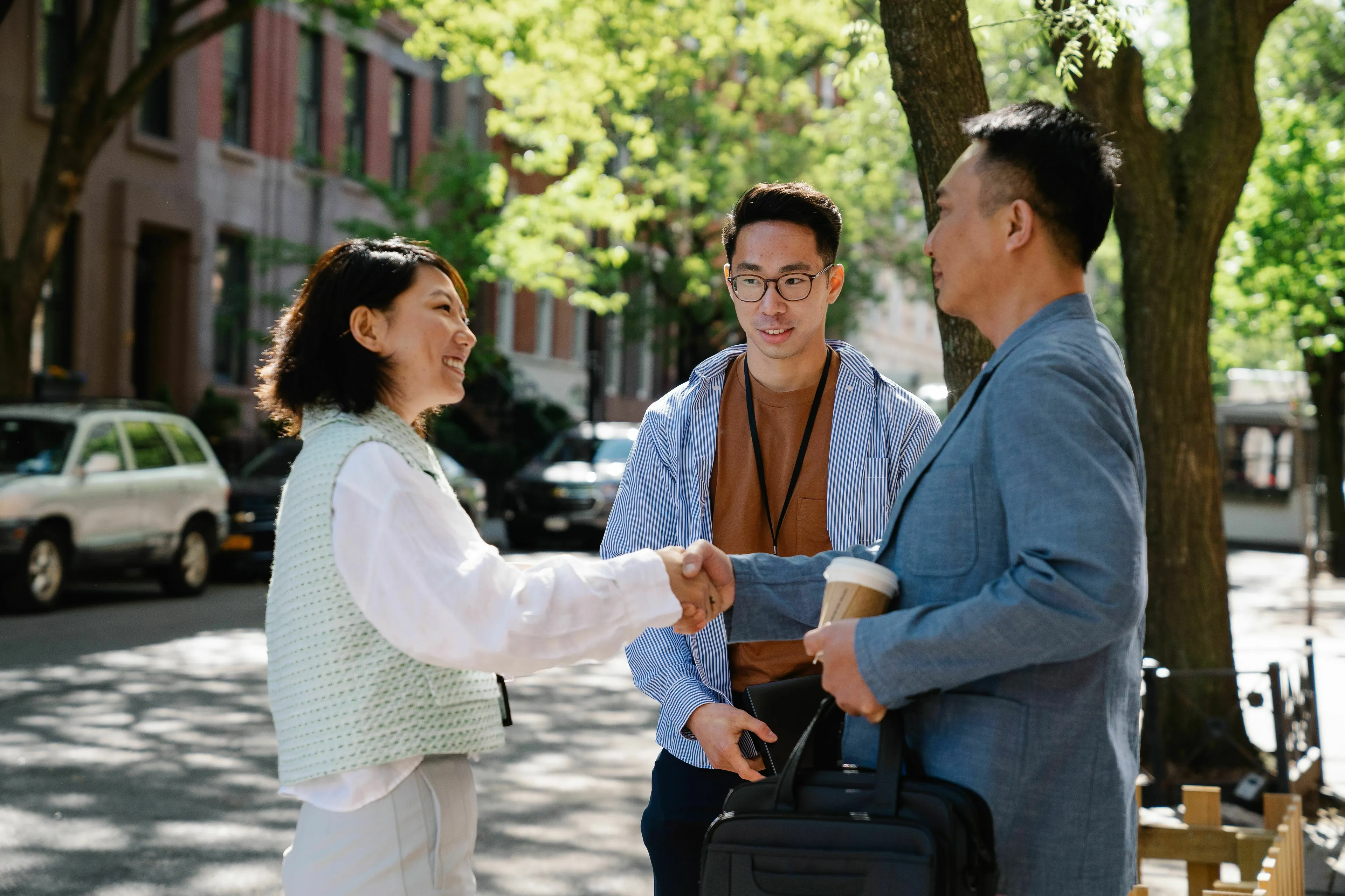 A new person joining a team is introduced, shaking hands with a colleague on a sunny street, a green flag for teamwork.