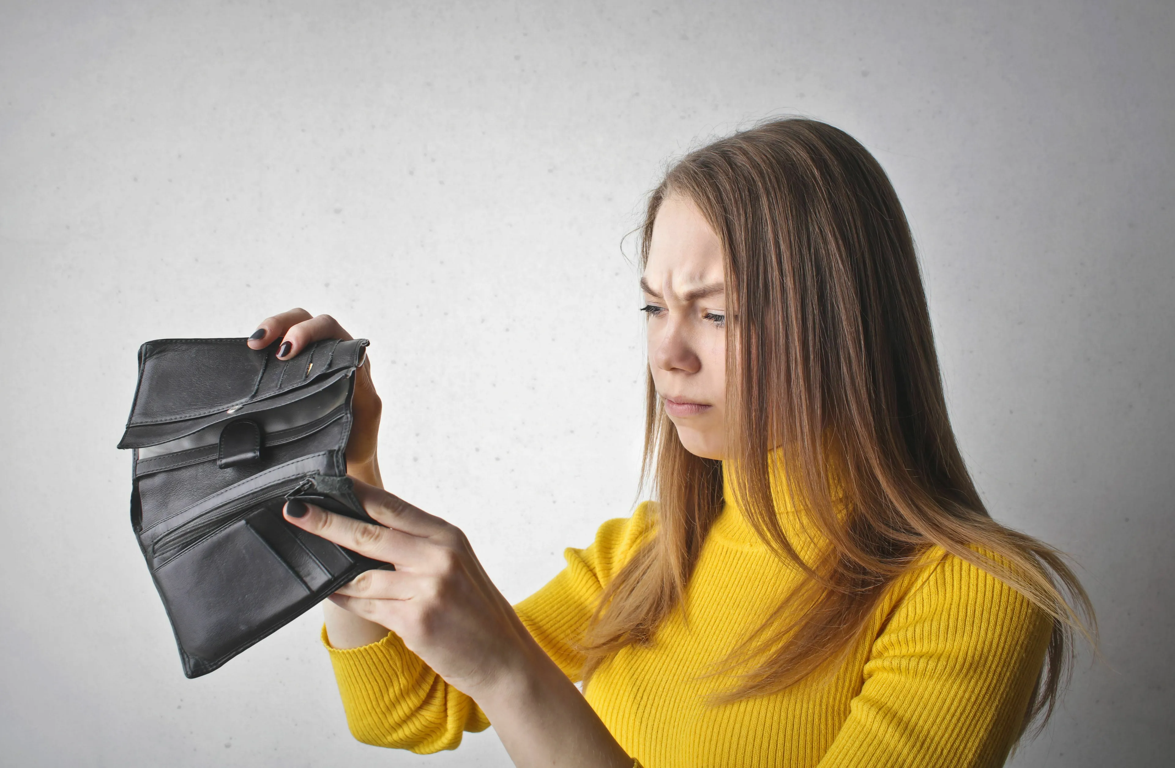A young woman looks worriedly at her empty wallet, depicting a green flag when a friend is in a financial rough spot.