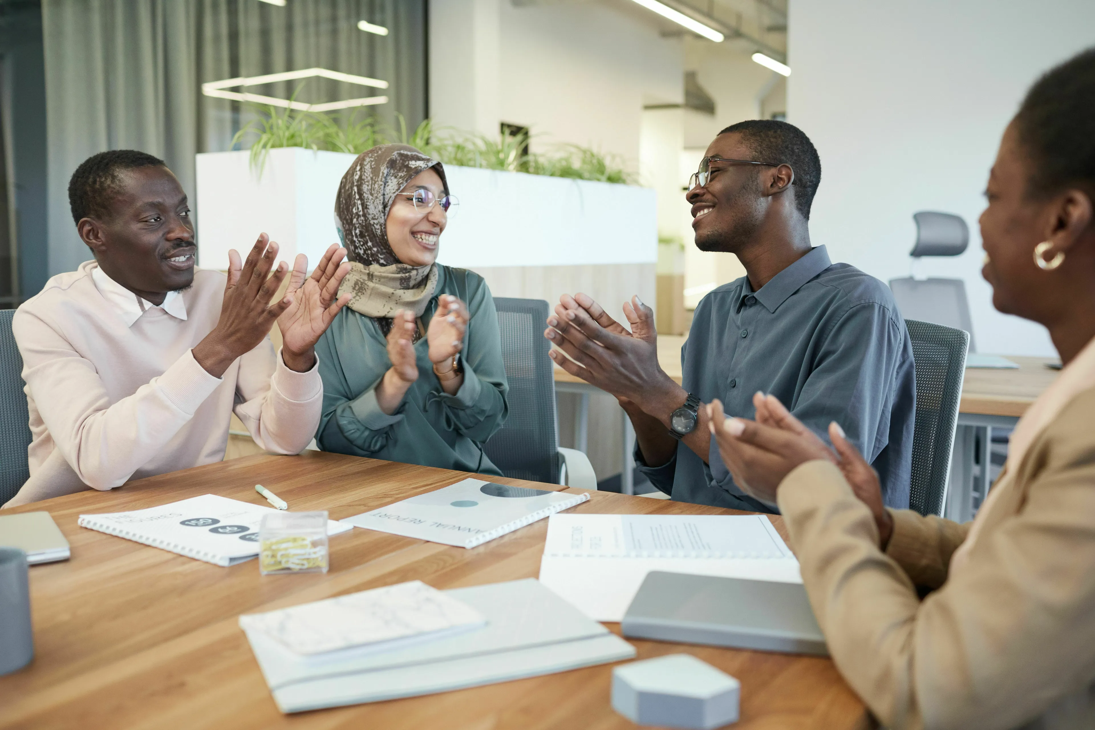 Four diverse individuals in a meeting clapping, symbolizing getting credit together for a green flag situation.