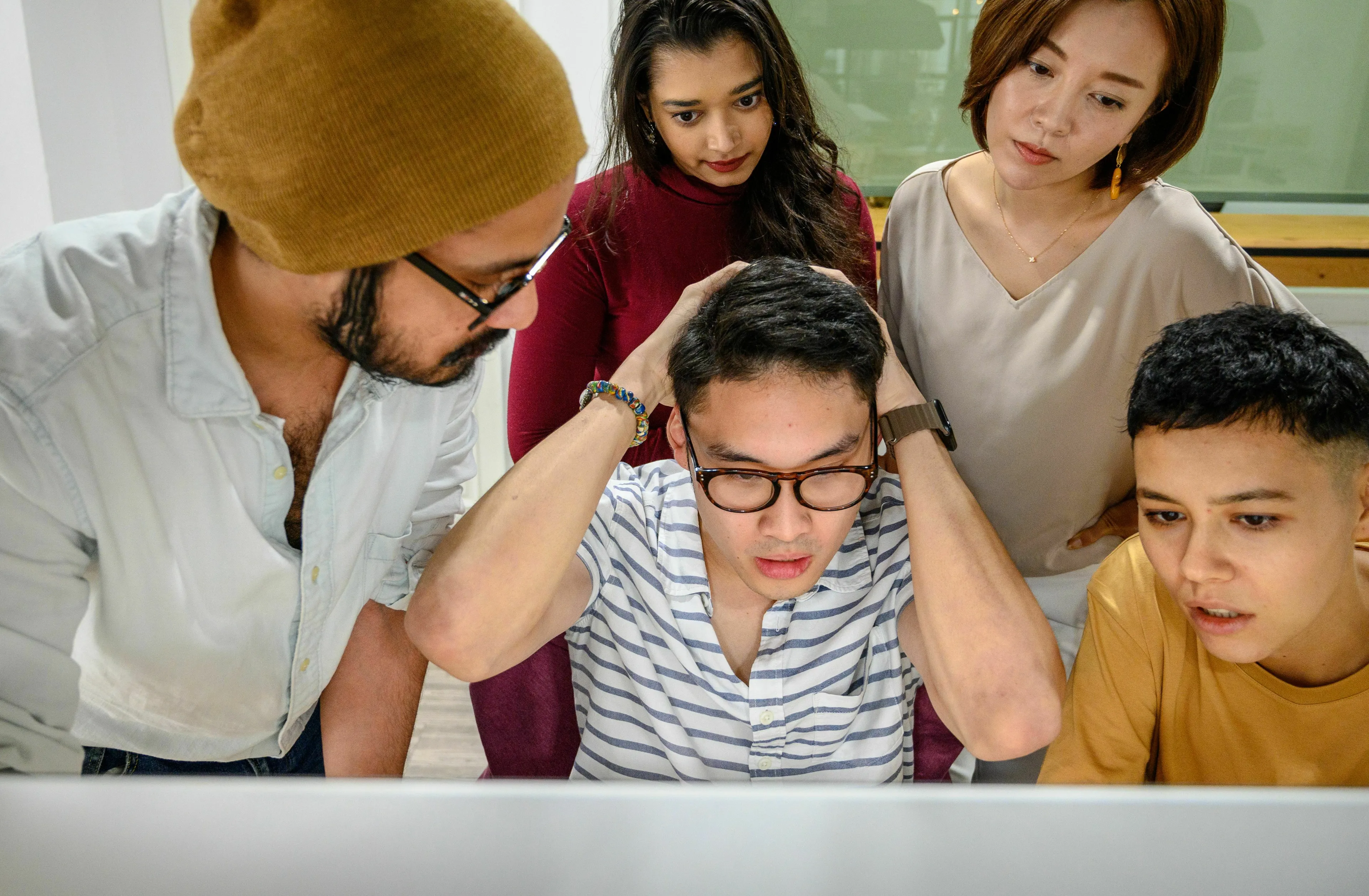 A group of people looking at a computer screen; one man holds his head, demonstrating a green flag for handling being wrong.