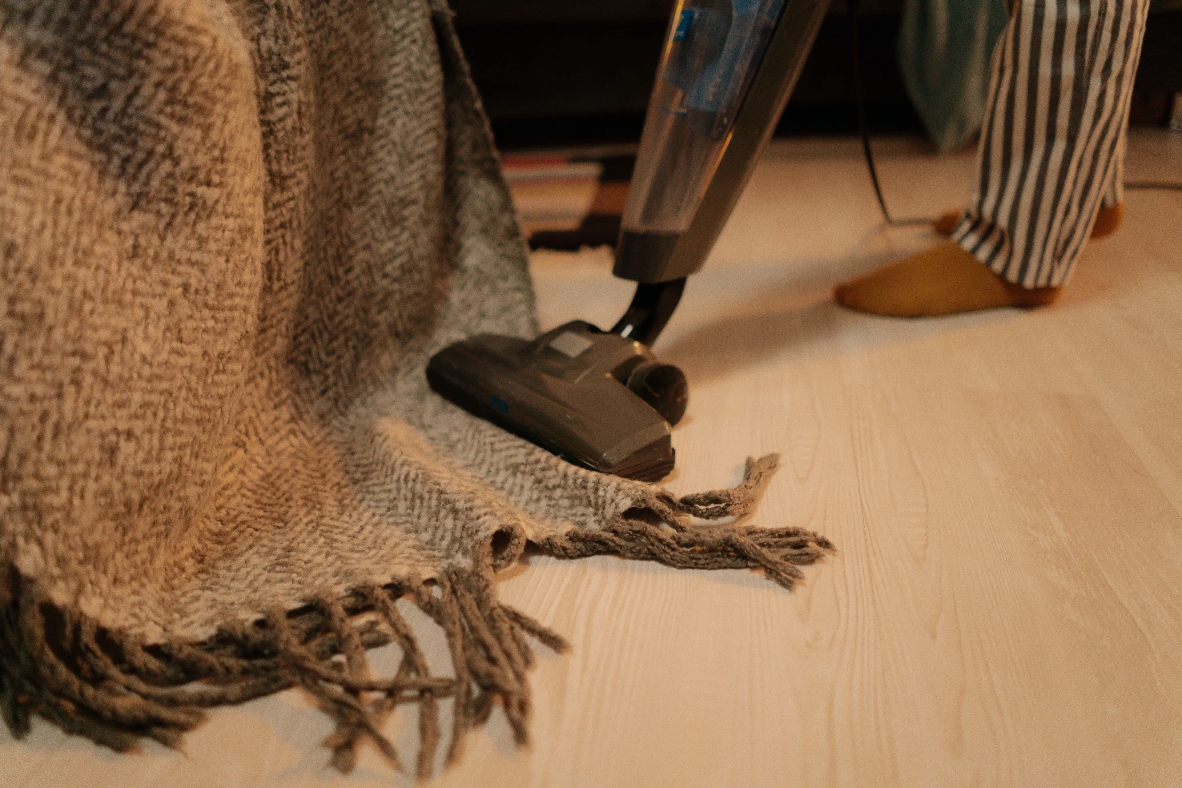 Last thing you do before bed: A person in striped pajamas vacuums a throw blanket on a light-colored floor, tidying the room.