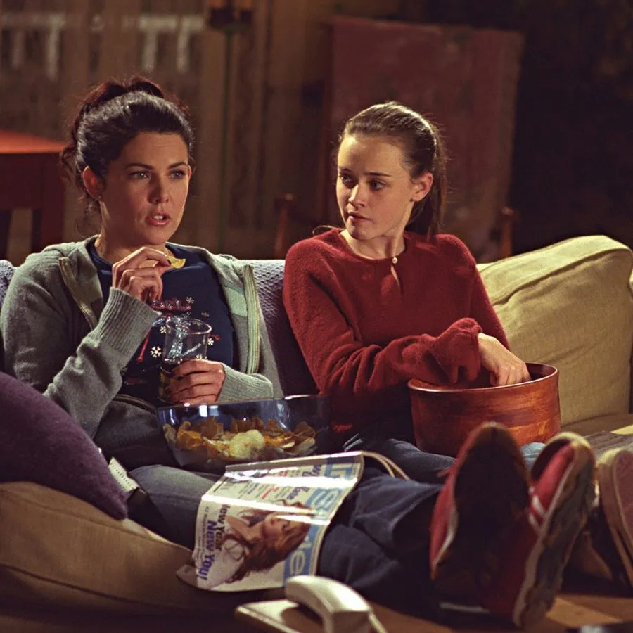 Lorelai and Rory Gilmore from Gilmore Girls relaxing on a couch, picking a comfort show.