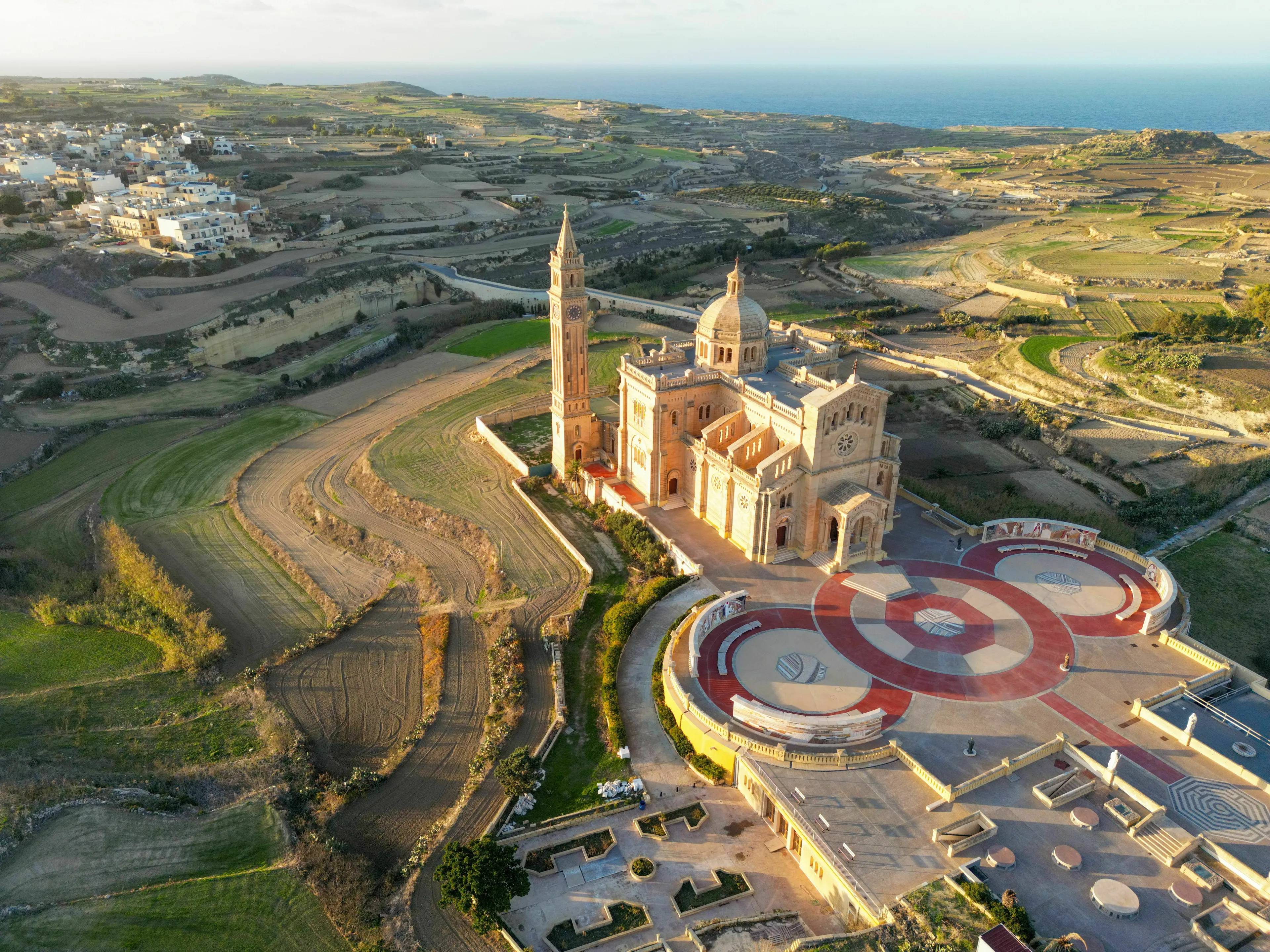 Aerial view of Ta Pinu Basilica on Gozo, part of an archipelago, set amidst cultivated terraced fields and the sea.