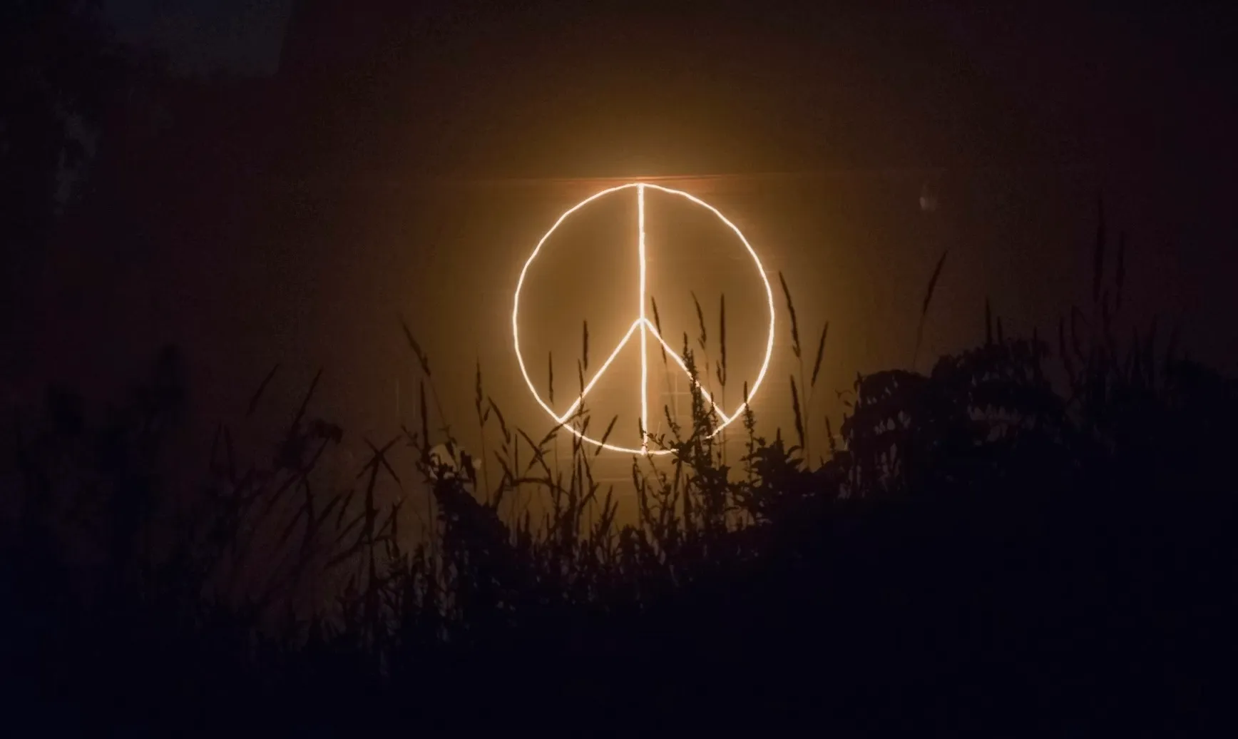 A glowing peace symbol at night, with dark grass and foliage silhouetted below. General Knowledge quiz.