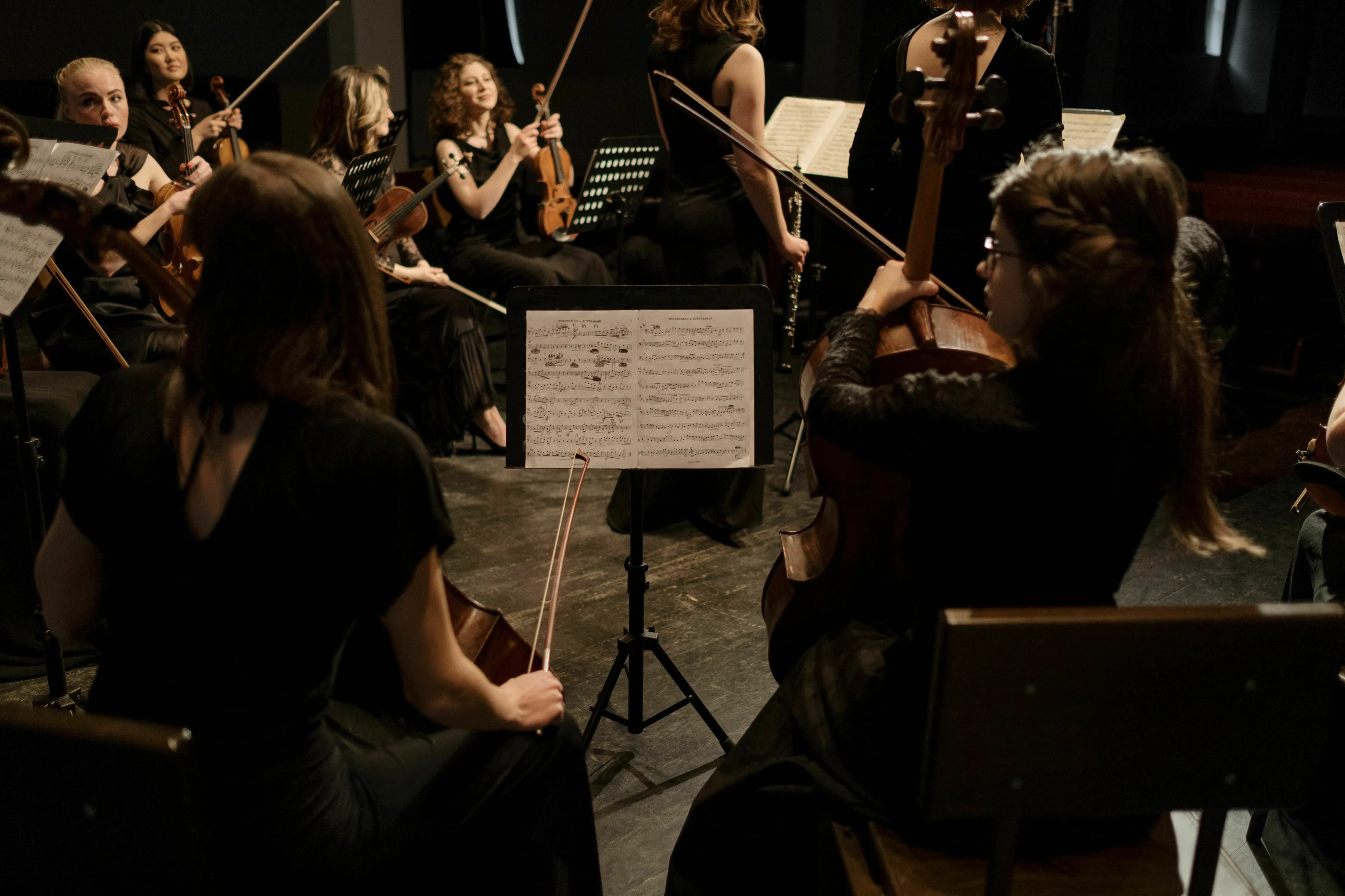 An orchestra performing, with a focus on a cello player, highlighting the number of strings on a standard cello.