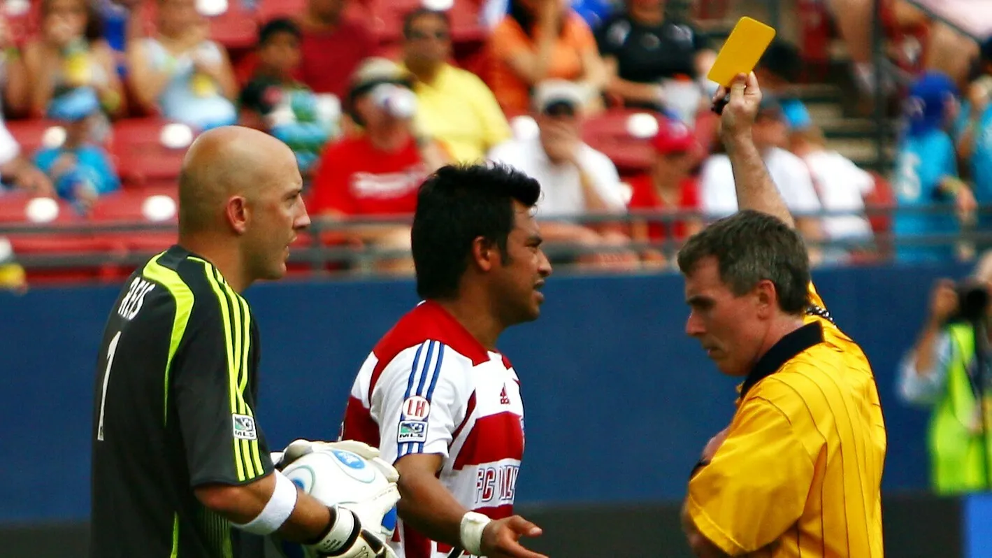 A referee showing a yellow card to a football player, with another player observing.