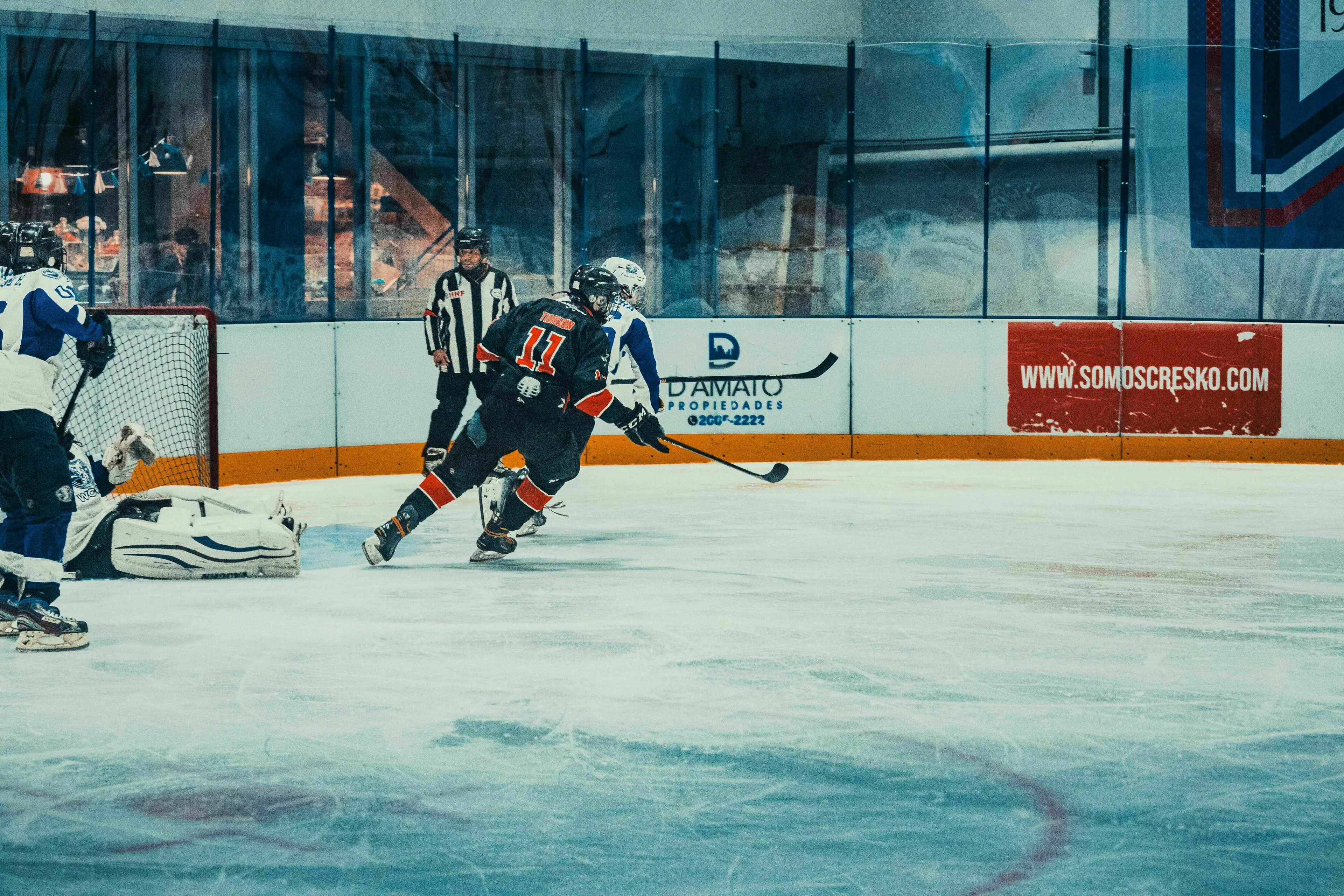 Ice hockey players on the ice during a game, actively playing with a goalie in front of the net.