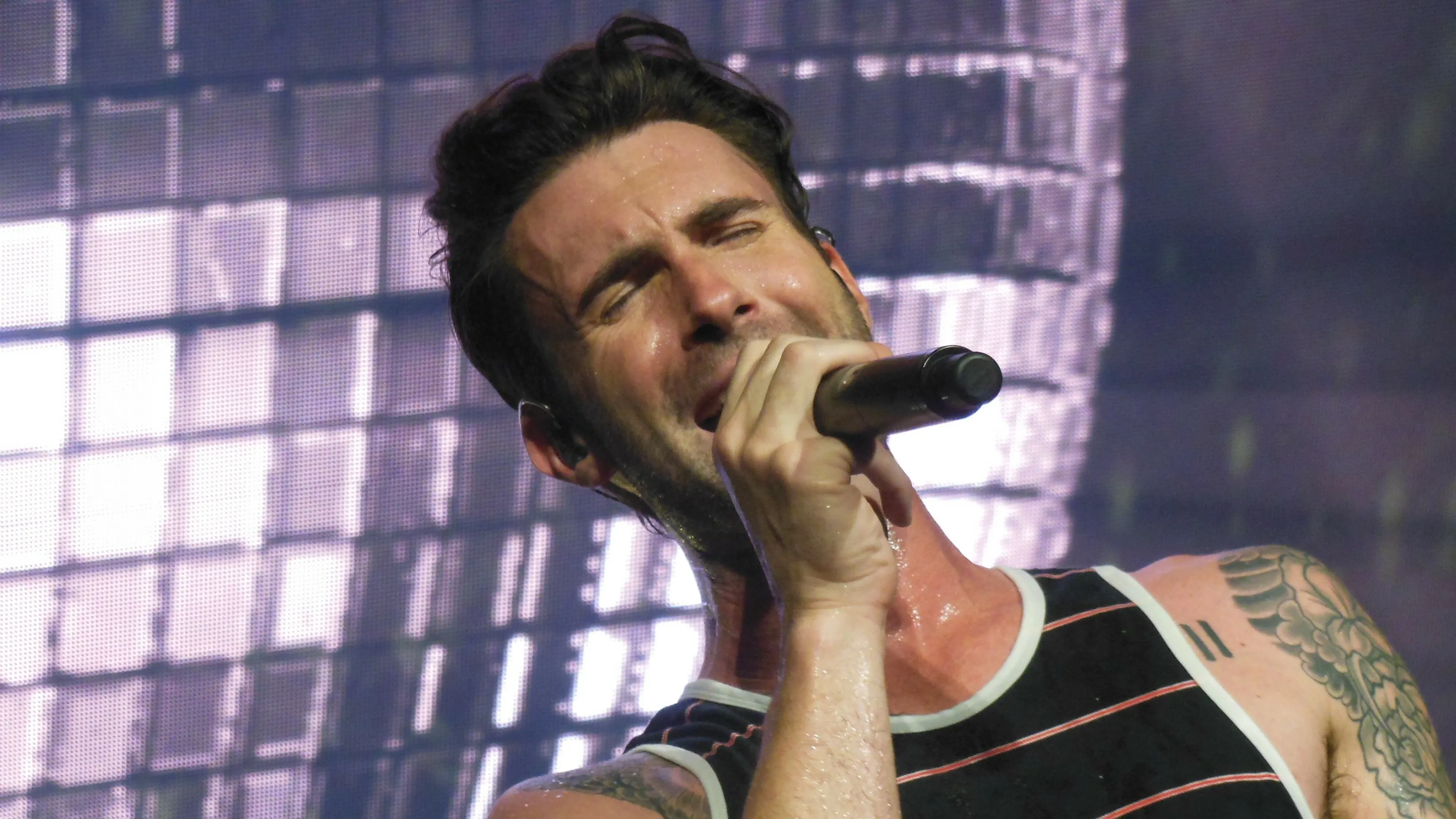 Adam Levine, frontman of a pop-rock band, singing intensely into a microphone on stage.