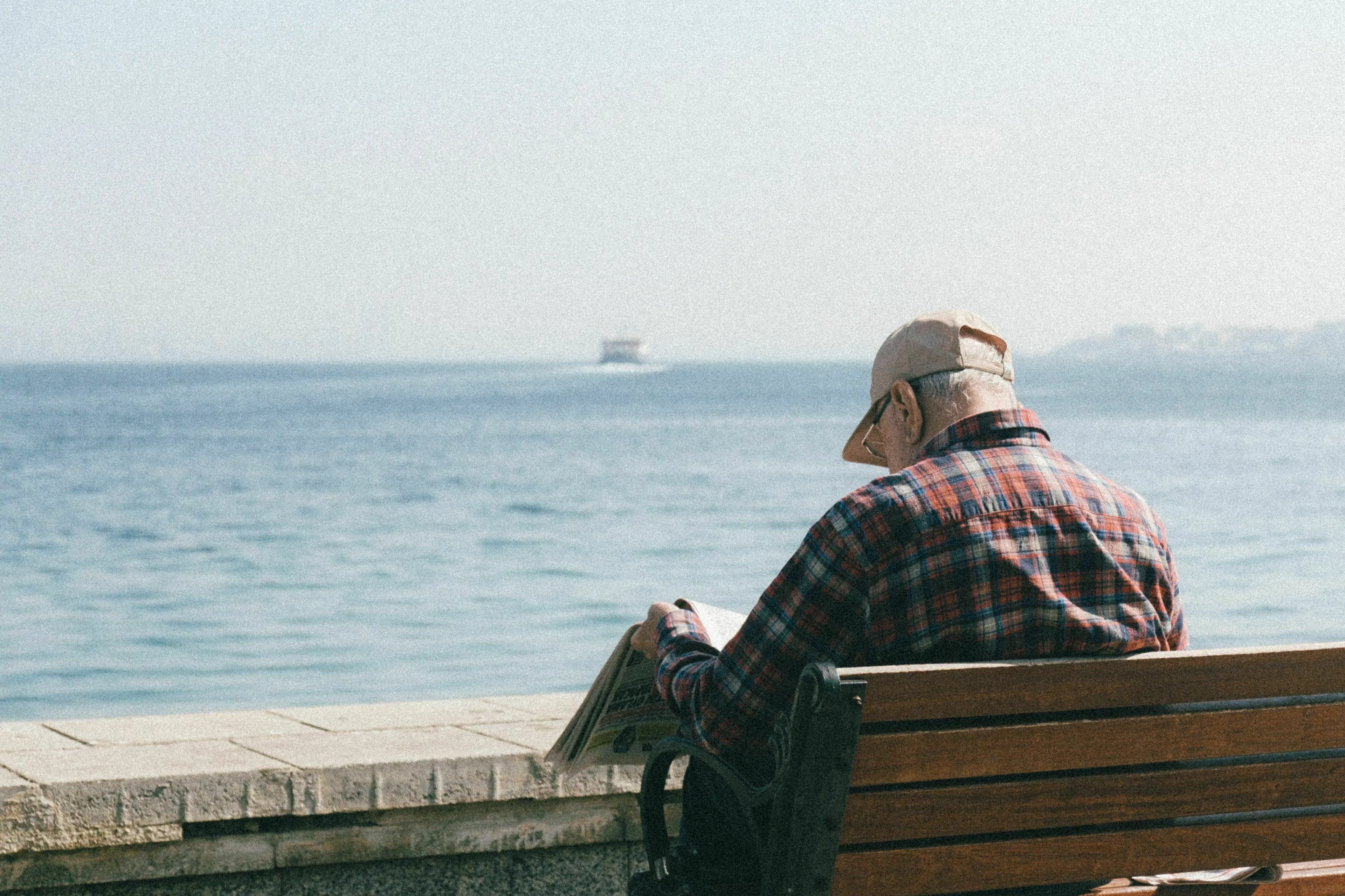 A man reading a newspaper by the sea, contemplating what triggers his envy of a neighbor who retired early.