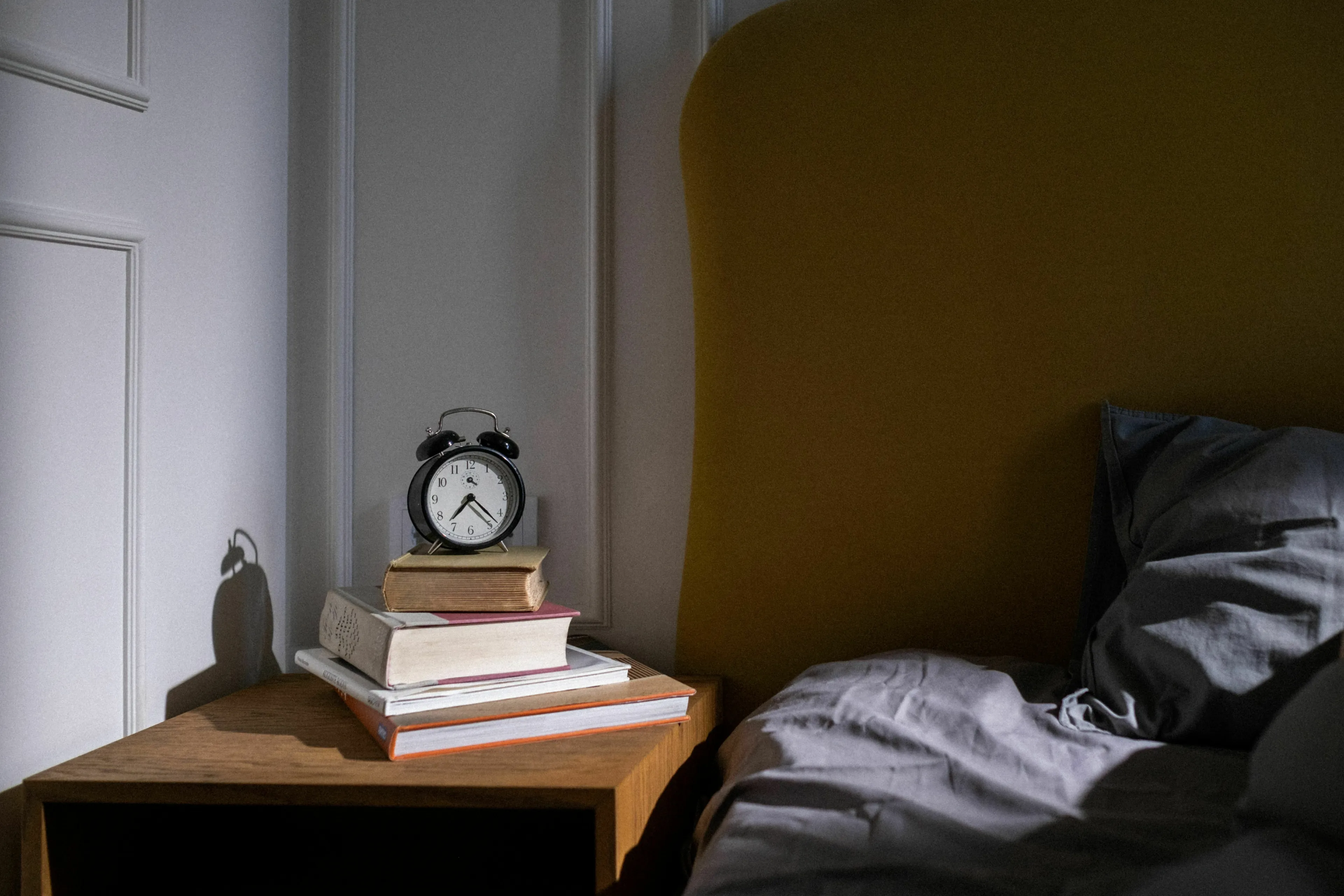 Alarm clock on books next to a bed, representing what triggers your envy first thing when you wake up.