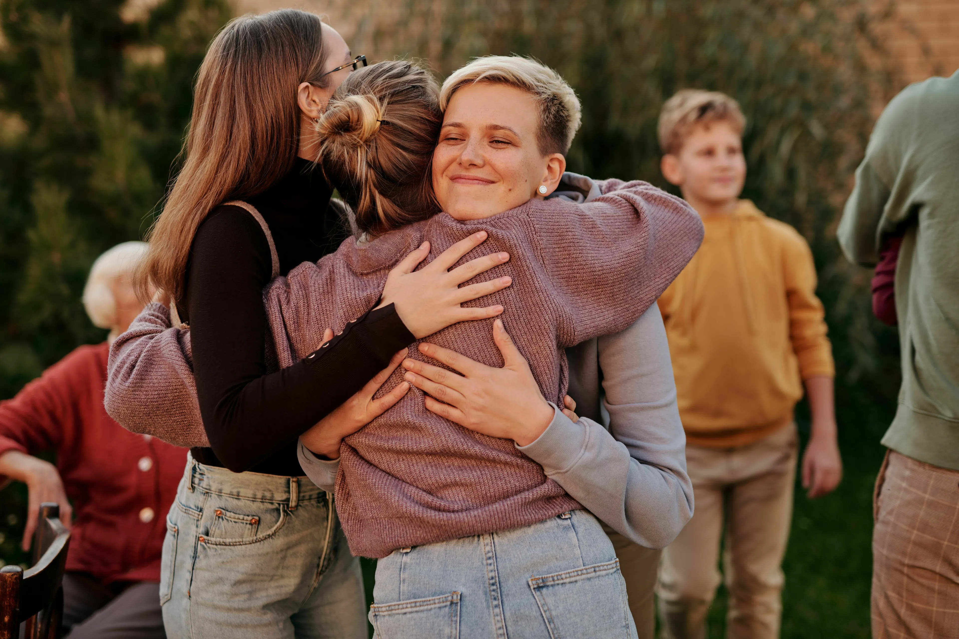 Avoiding someone at a reunion, with three people embracing warmly in a group, while others stand in the background.