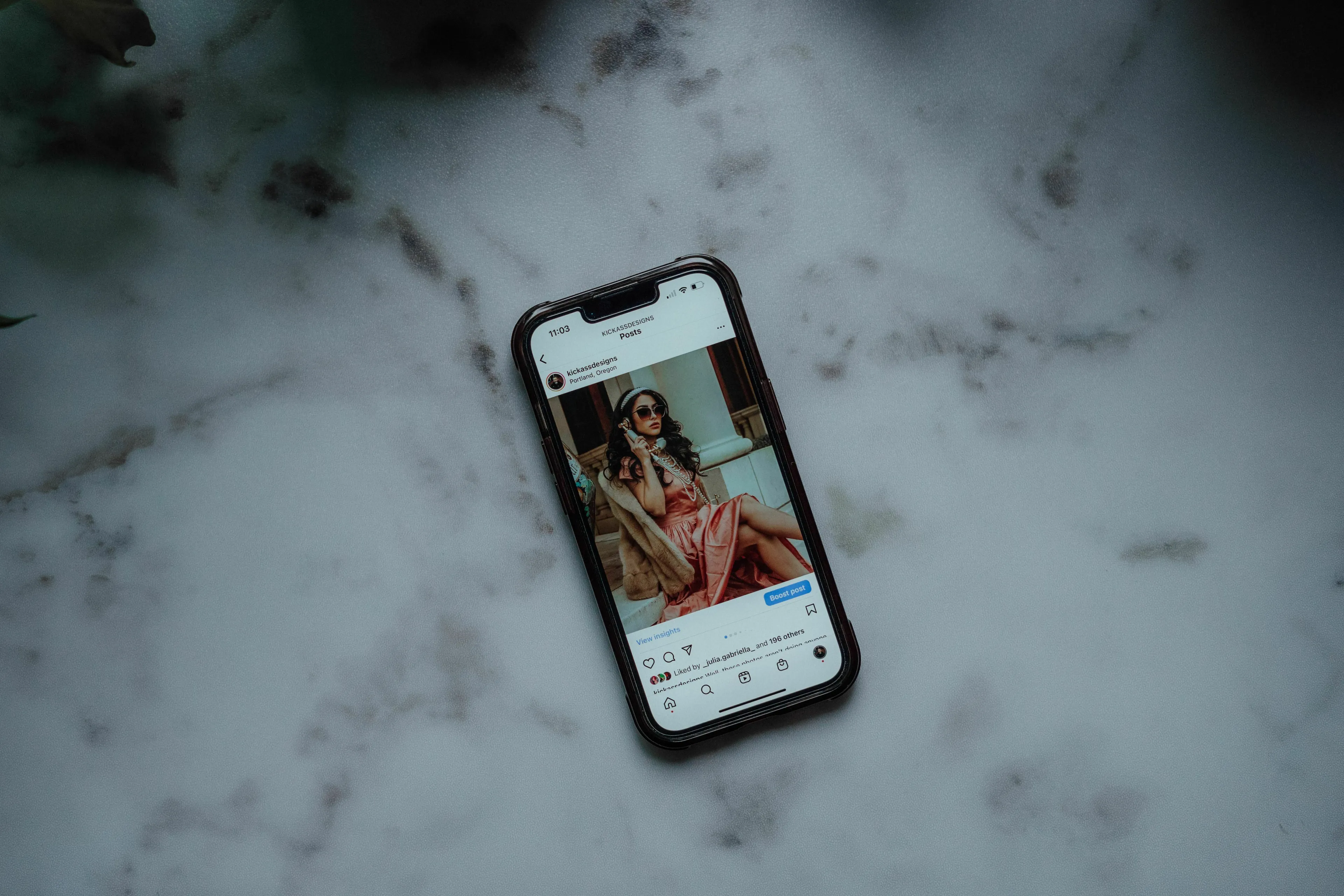 A smartphone displaying a social media post of a woman in a pink dress on a marble surface. Triggers envy on social media posts.