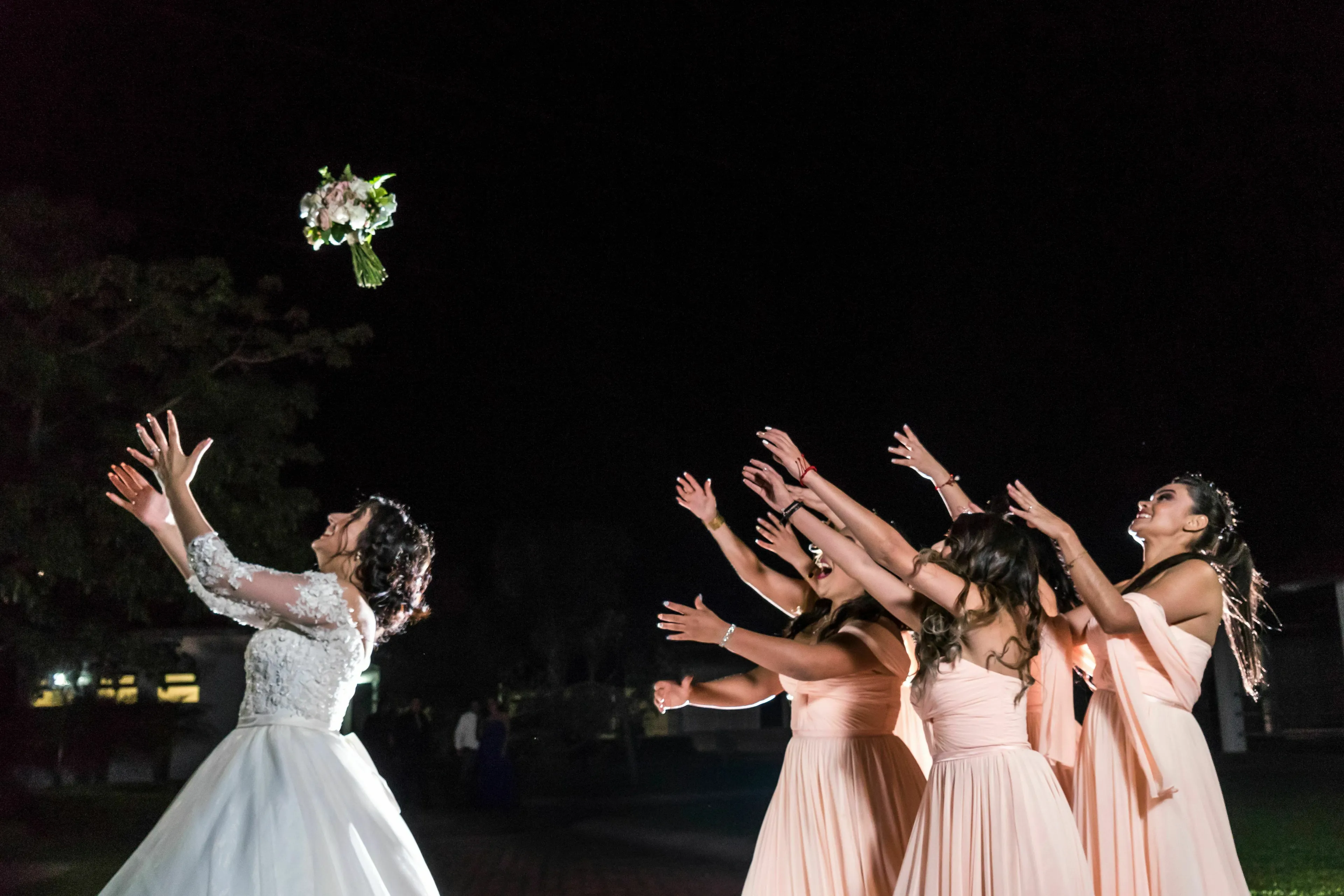 A bride throws her wedding bouquet to a group of bridesmaids and guests, triggering envy.