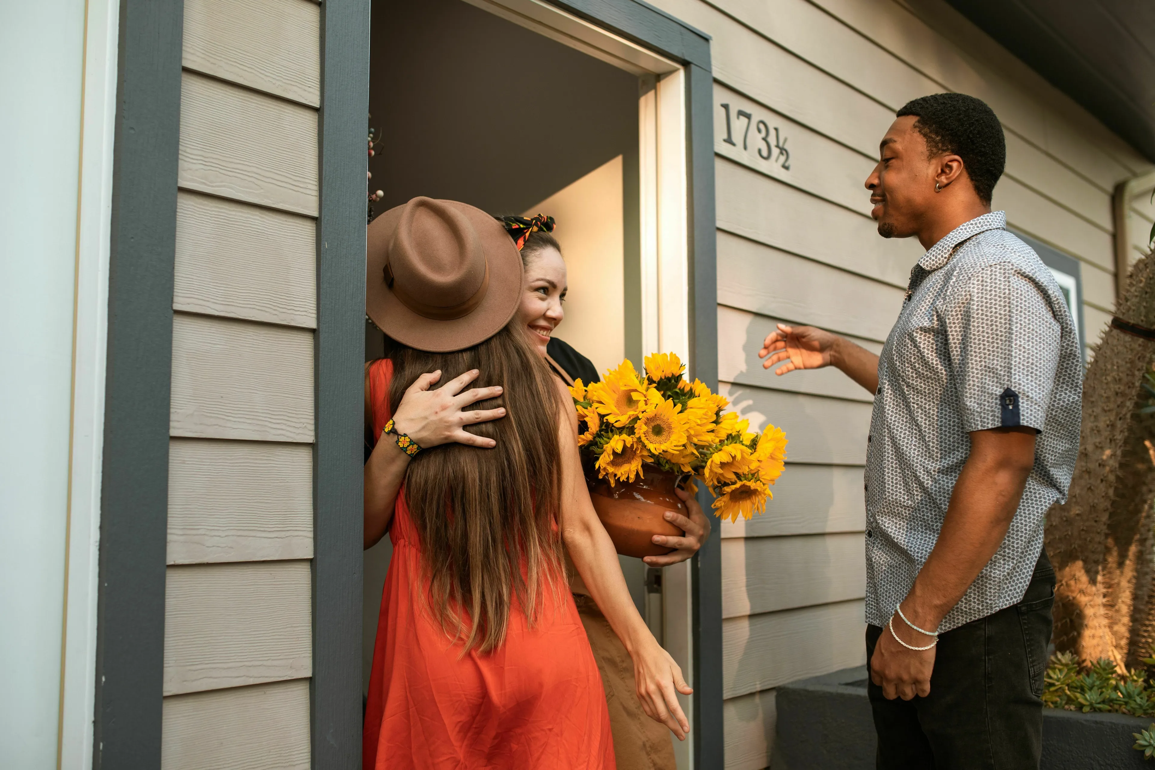 A woman arriving at a housewarming party, holding sunflowers and embracing a friend, exploring triggers for envy.