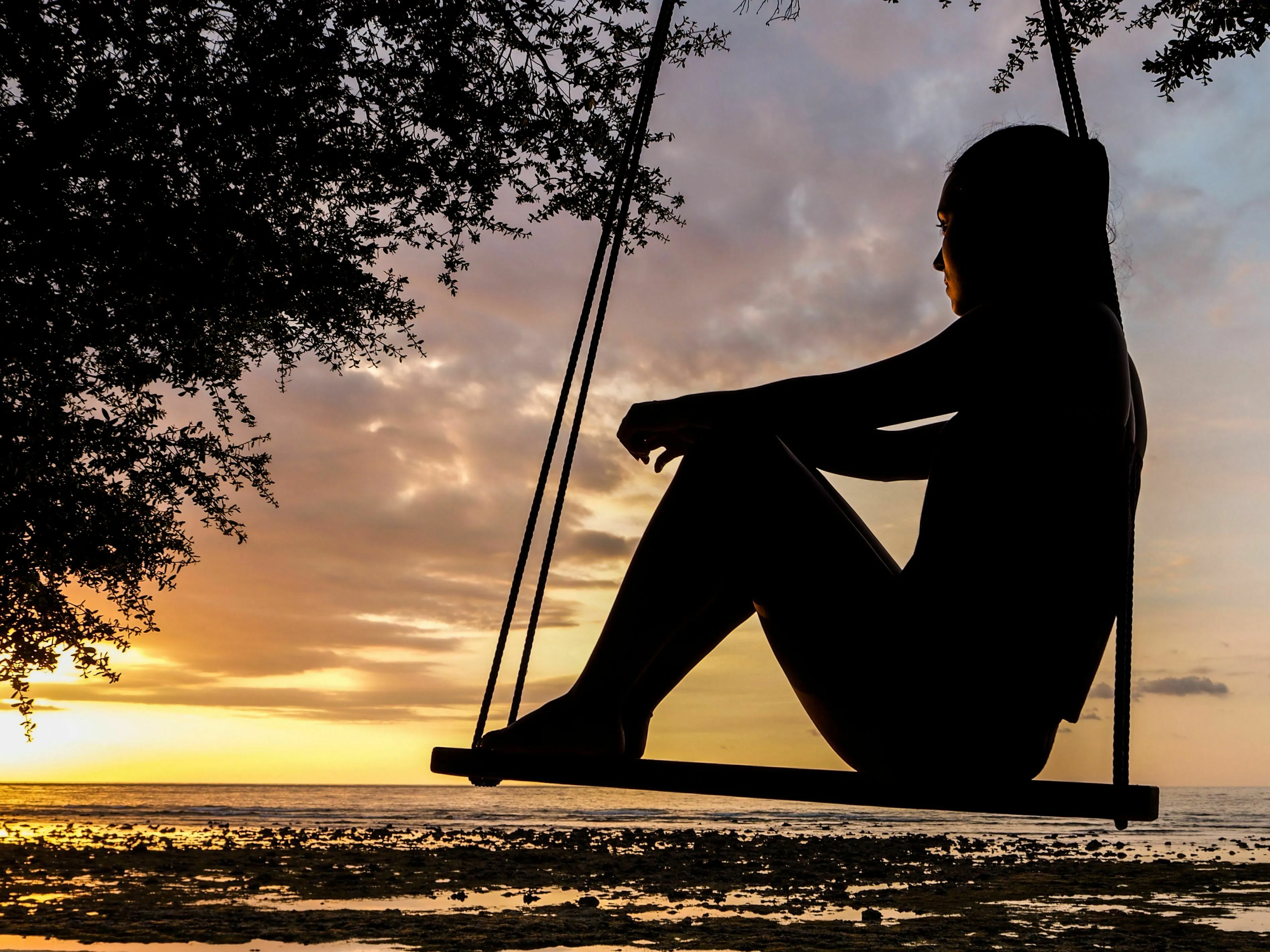Silhouette of a person on a swing over water at sunset, pondering what triggers your envy.