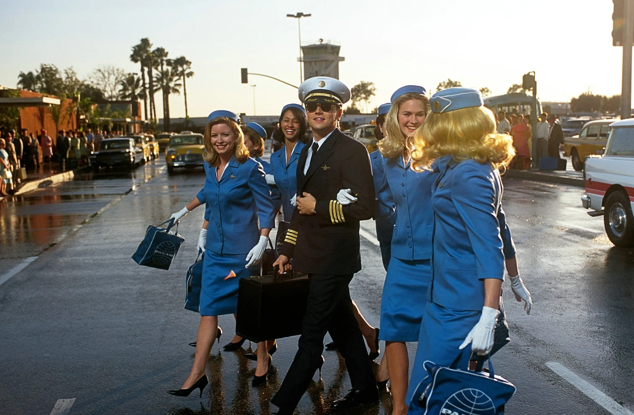 Leonardo DiCaprio portraying Frank Abagnale Jr. from Catch Me If You Can, walking with flight attendants on a lazy Sunday.
