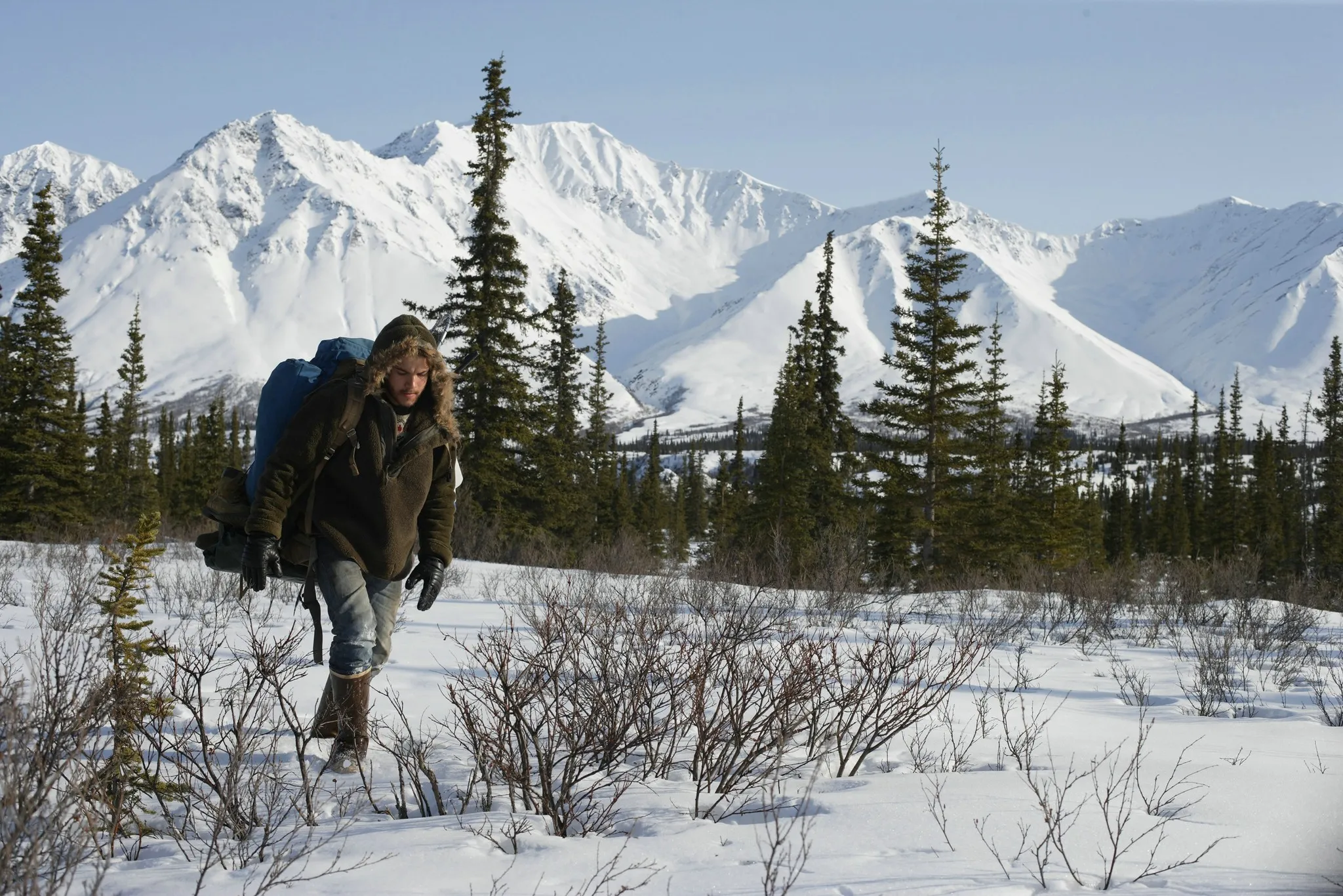A man with a backpack walking through a snowy landscape from Into the Wild, set against mountains on a lazy Sunday.