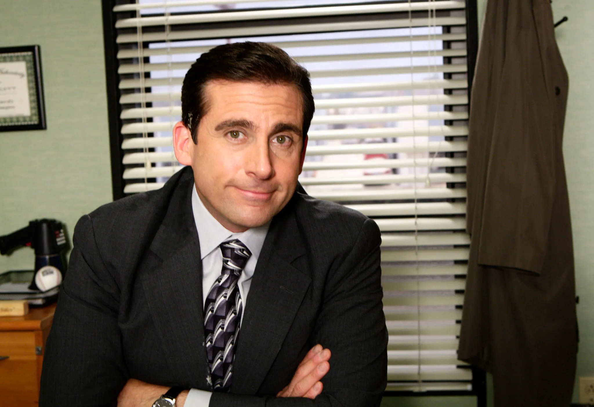 Michael Scott from The Office, seated at his desk with arms crossed and a slight smile, a fictional character to low-key envy.