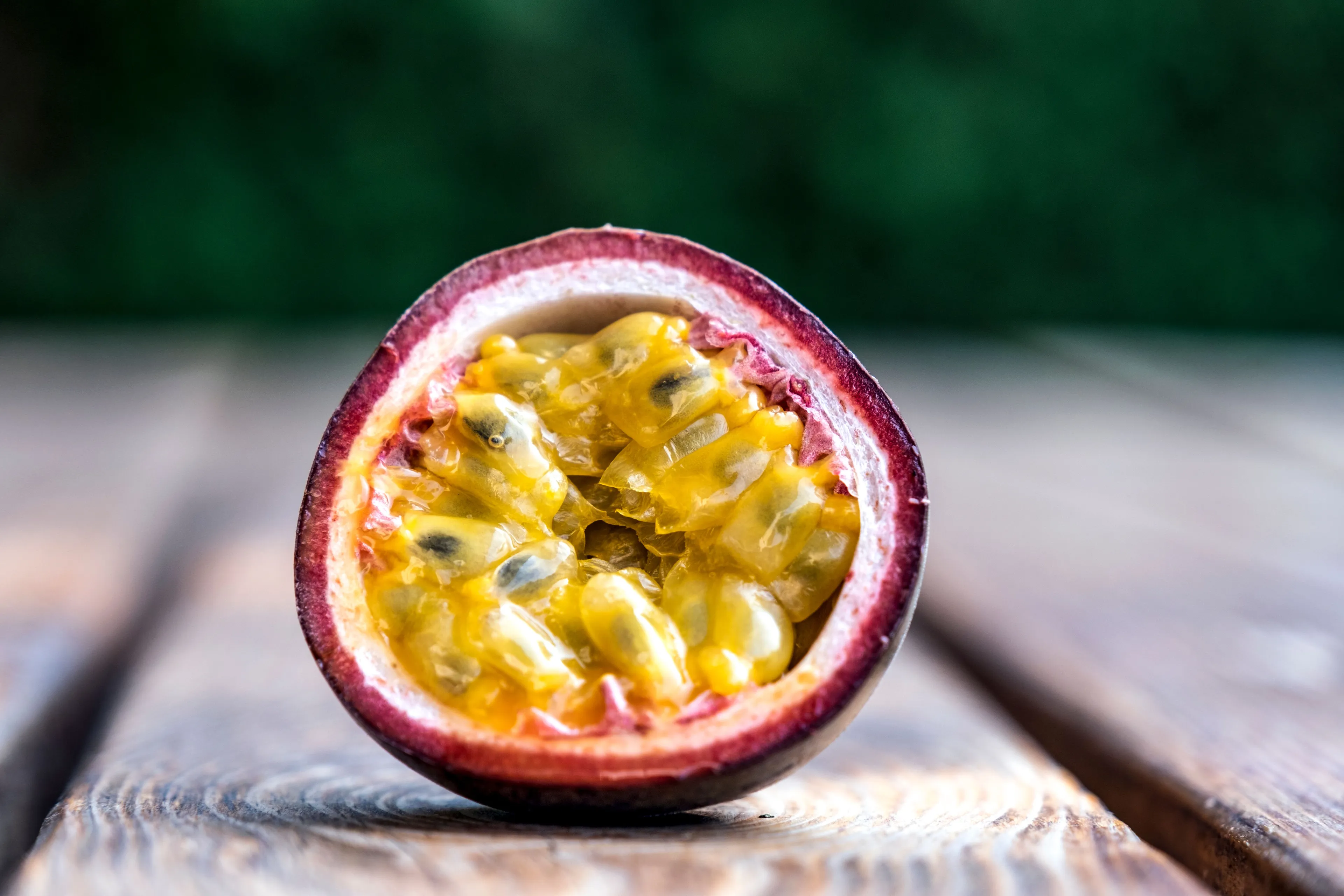 A vibrant passion fruit cut in half, showcasing its juicy, seed-filled yellow pulp on a rustic wooden table.