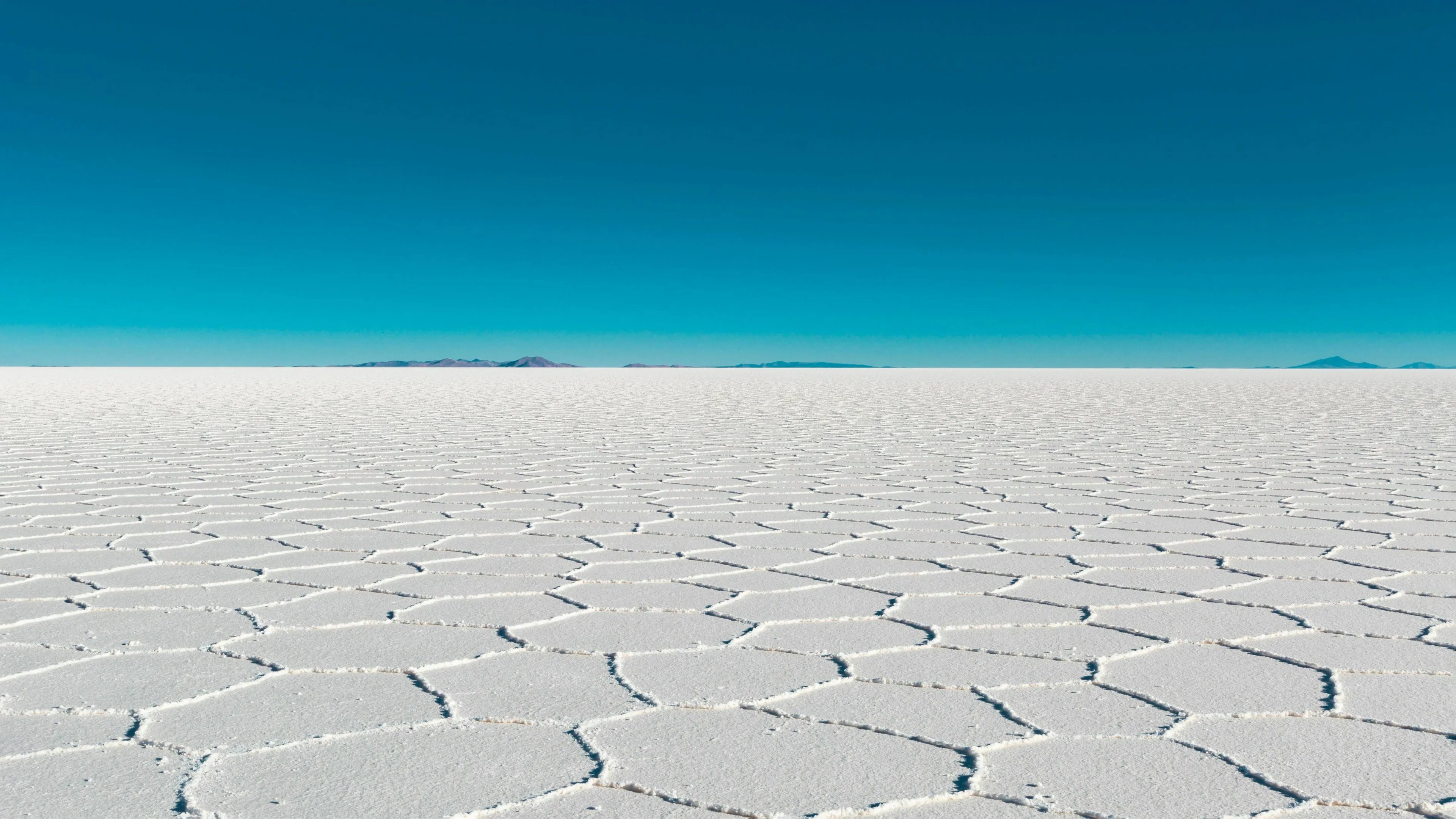 Vast, white, hexagonal patterns of the Salar de Uyuni, the worlds largest salt flat, under a clear blue sky.
