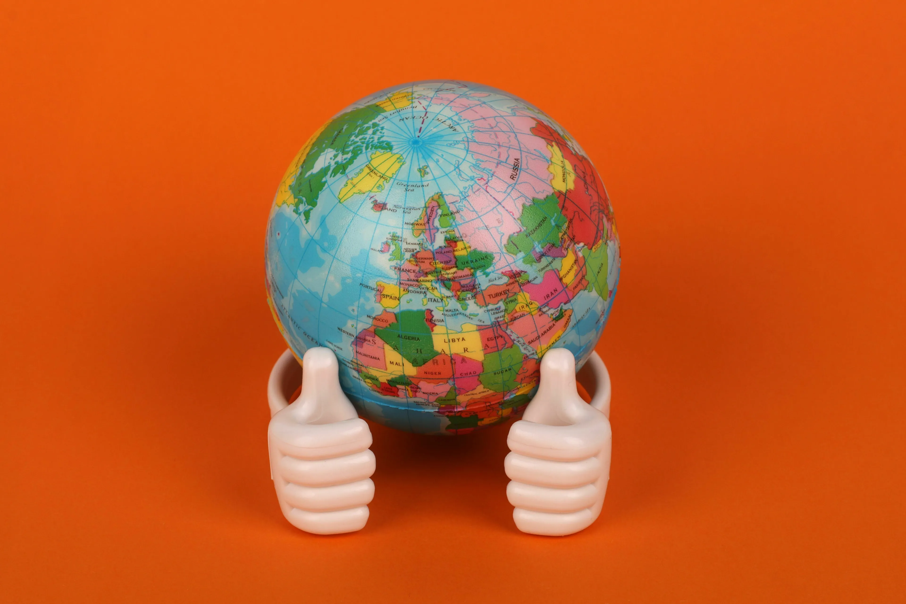 A globe displaying land masses surrounded by water, with two thumbs-up hands supporting it, representing general geography knowledge.