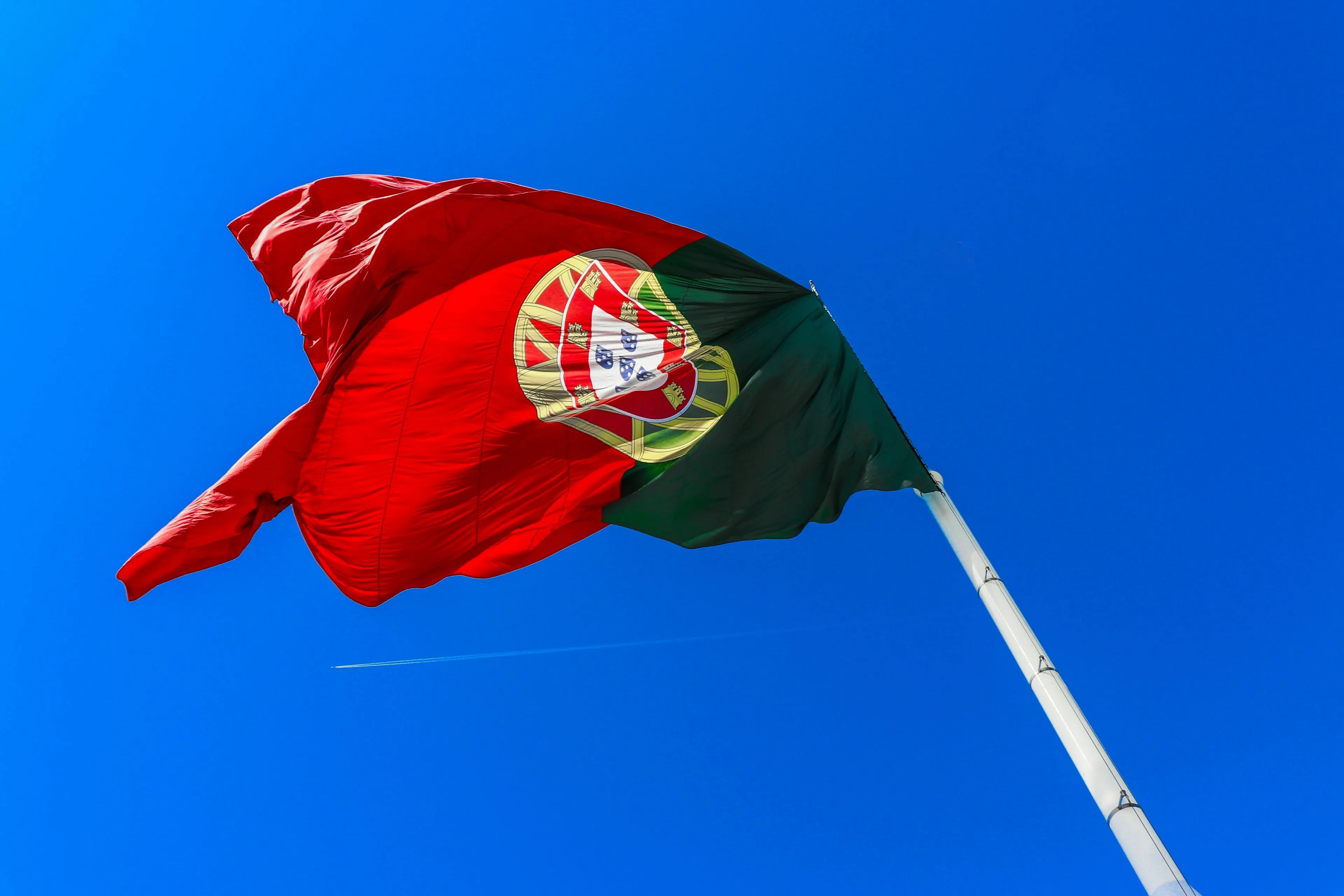 The flag of Portugal waving against a blue sky, representing a geography quiz question about its capital city.