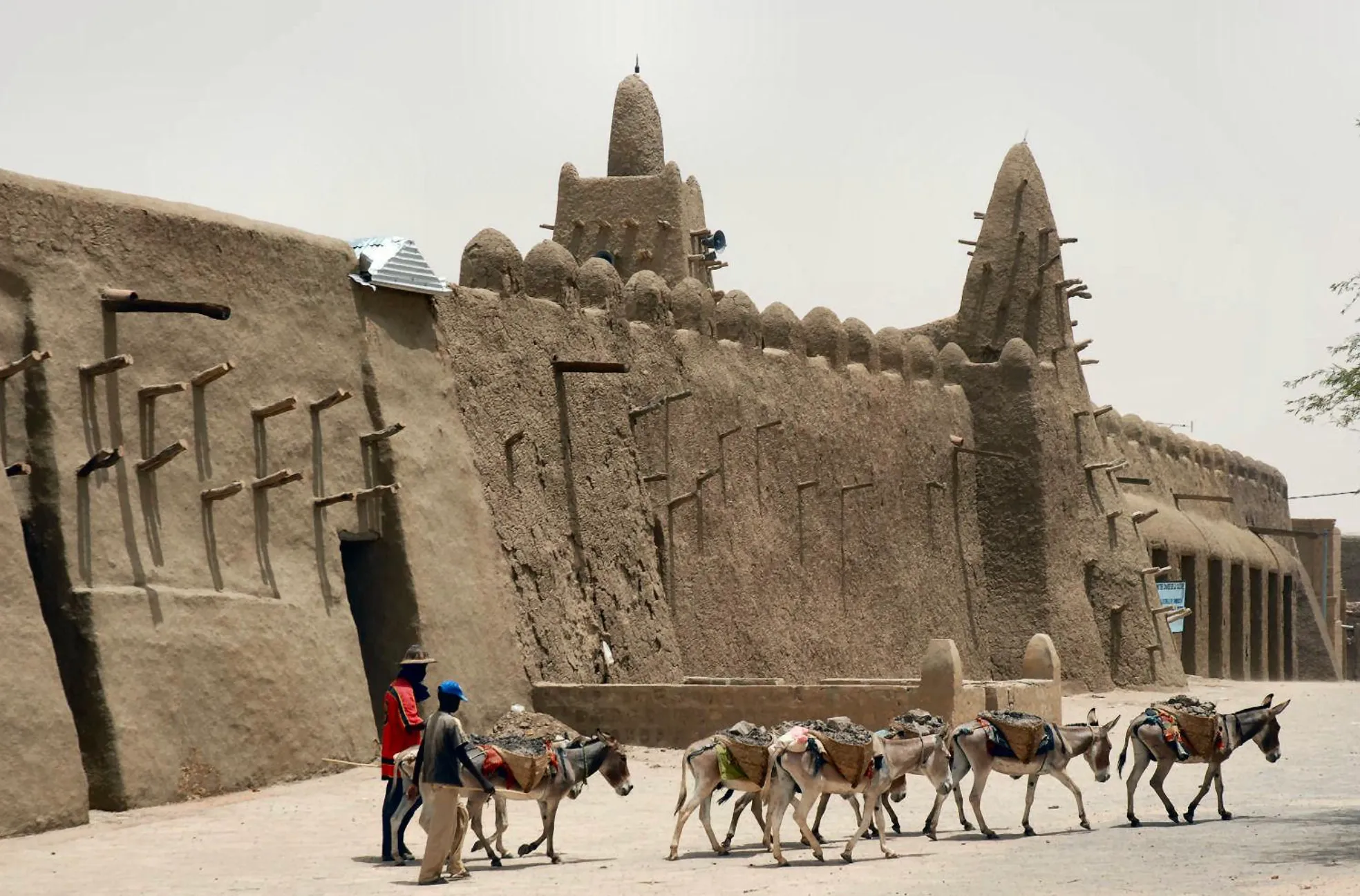 Ancient mud-brick buildings of Timbuktu, Mali, with people and donkeys in the foreground. General geography knowledge quiz.