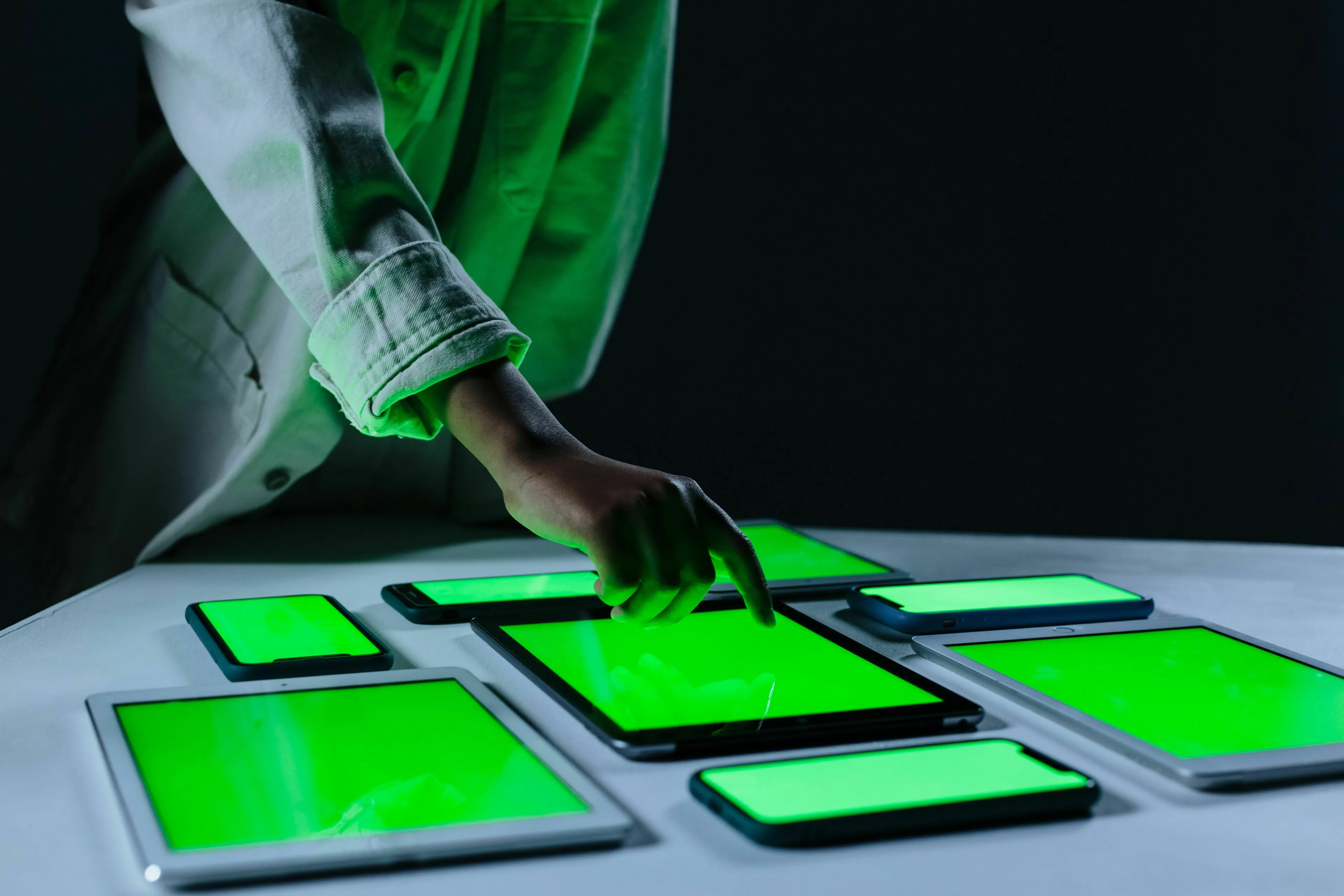 A person interacts with multiple glowing green screens of new technology, embodying how they feel about it for the decade they were born to live in.