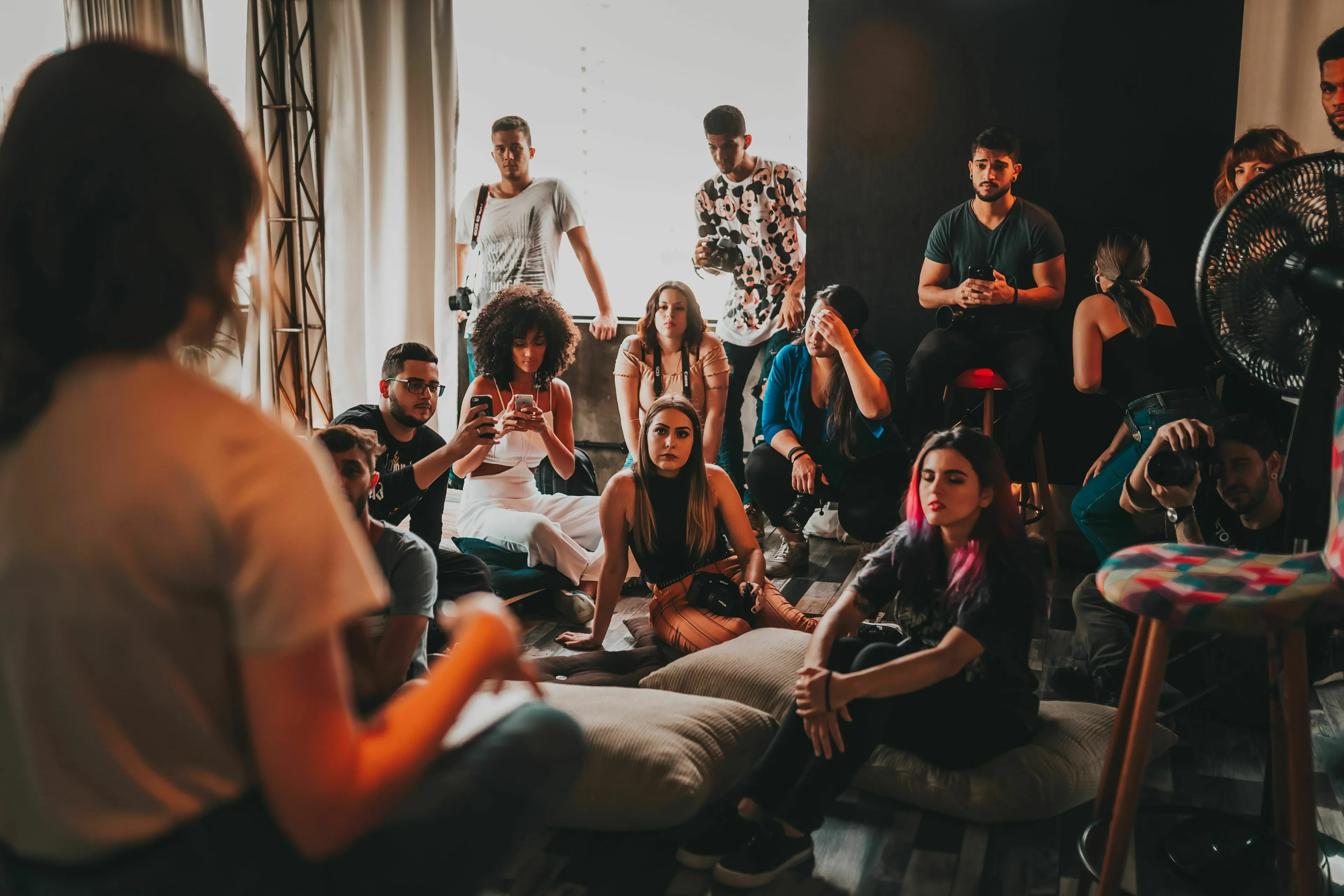 A group of people are gathered, some sitting on pillows, some standing, engaged in a discussion, illustrating a good gathering and which decade they were born for.