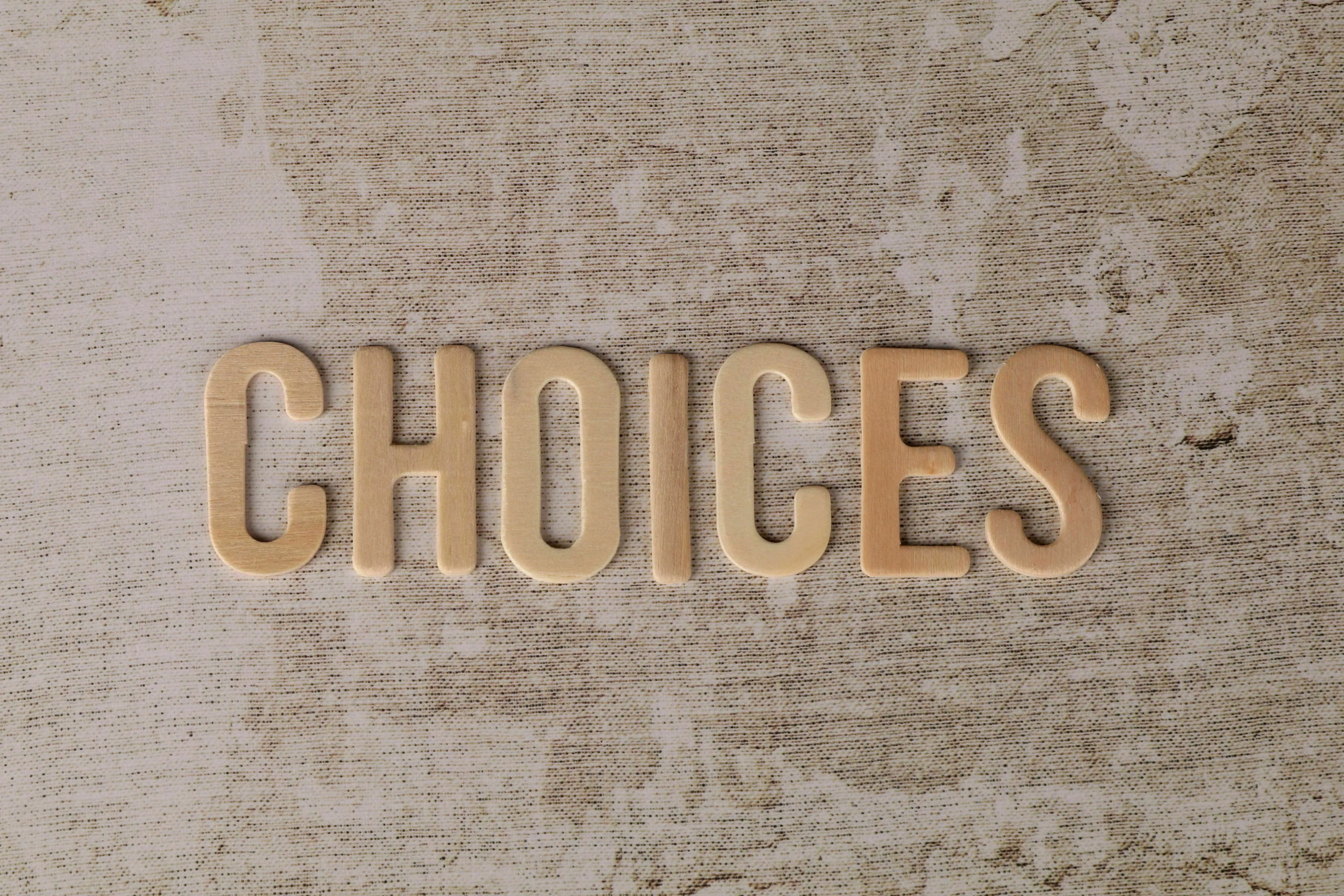 Wooden letters spelling out CHOICES on a textured background, representing making big decisions and the decade you were born to live in.