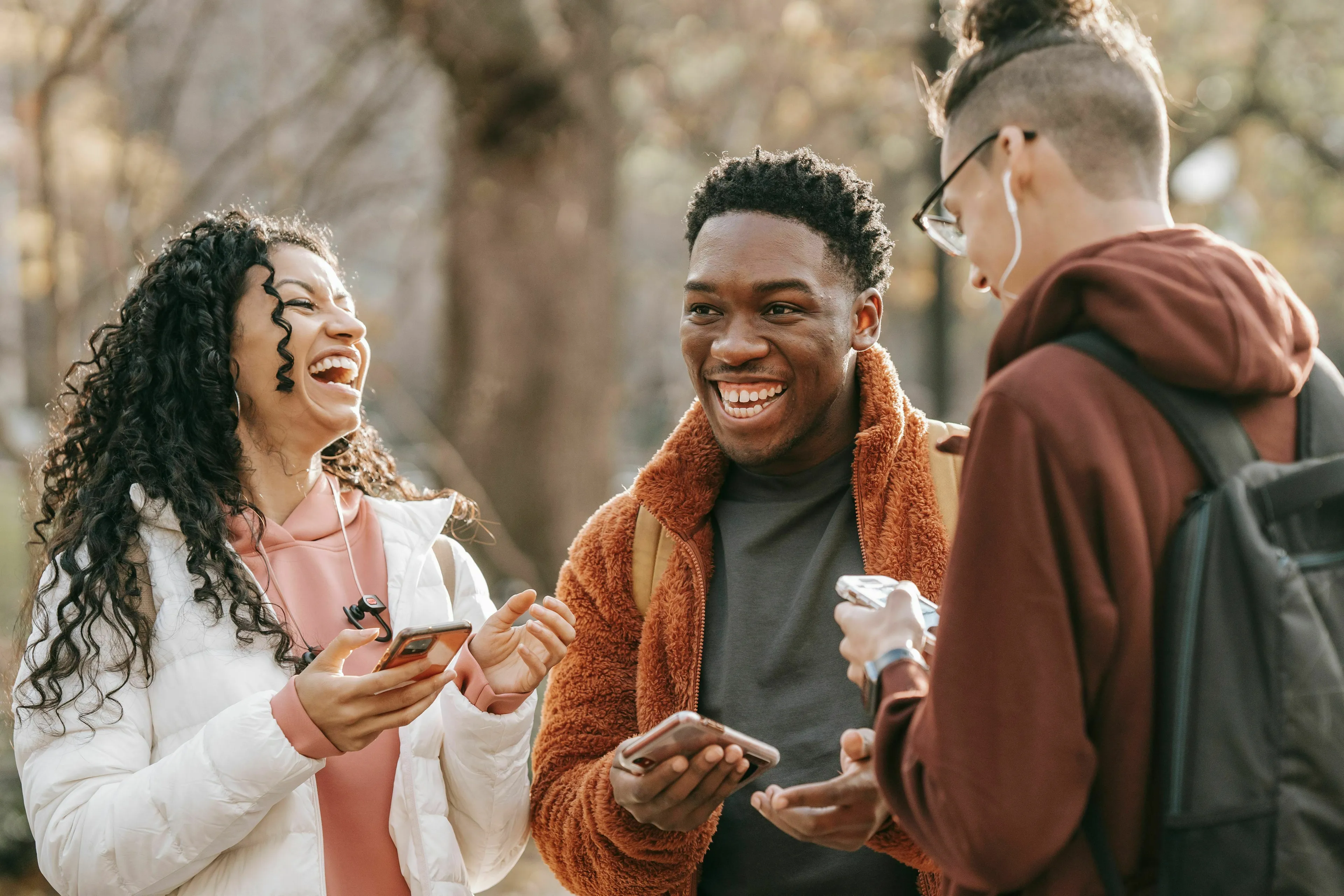 Three young friends laughing and smiling while looking at their phones, showing what they value most in a friend for the decade they were born for.