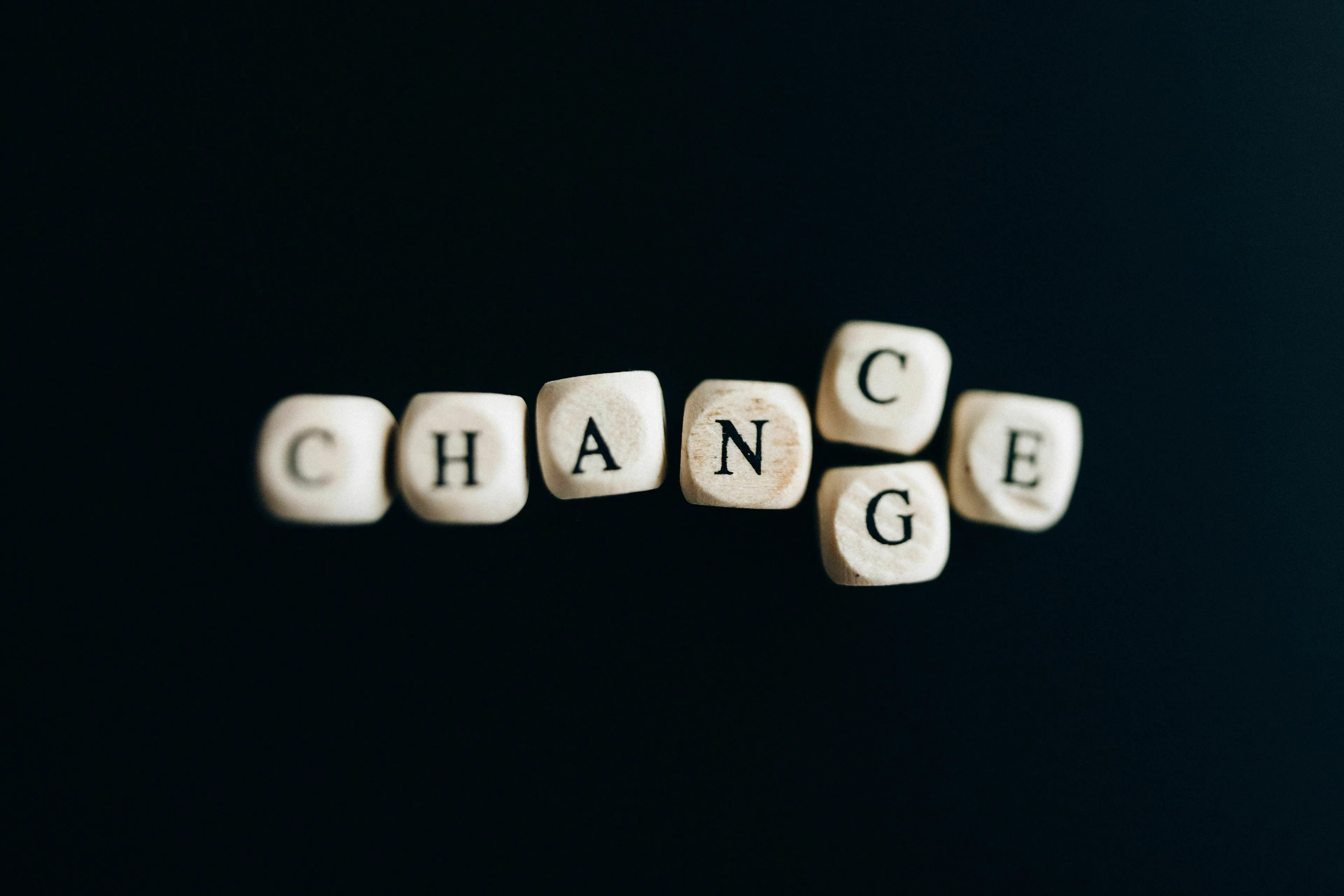 Wooden letter cubes spelling out the word CHANGE on a dark background, depicting how one reacts to sudden change and the decade they were born for.