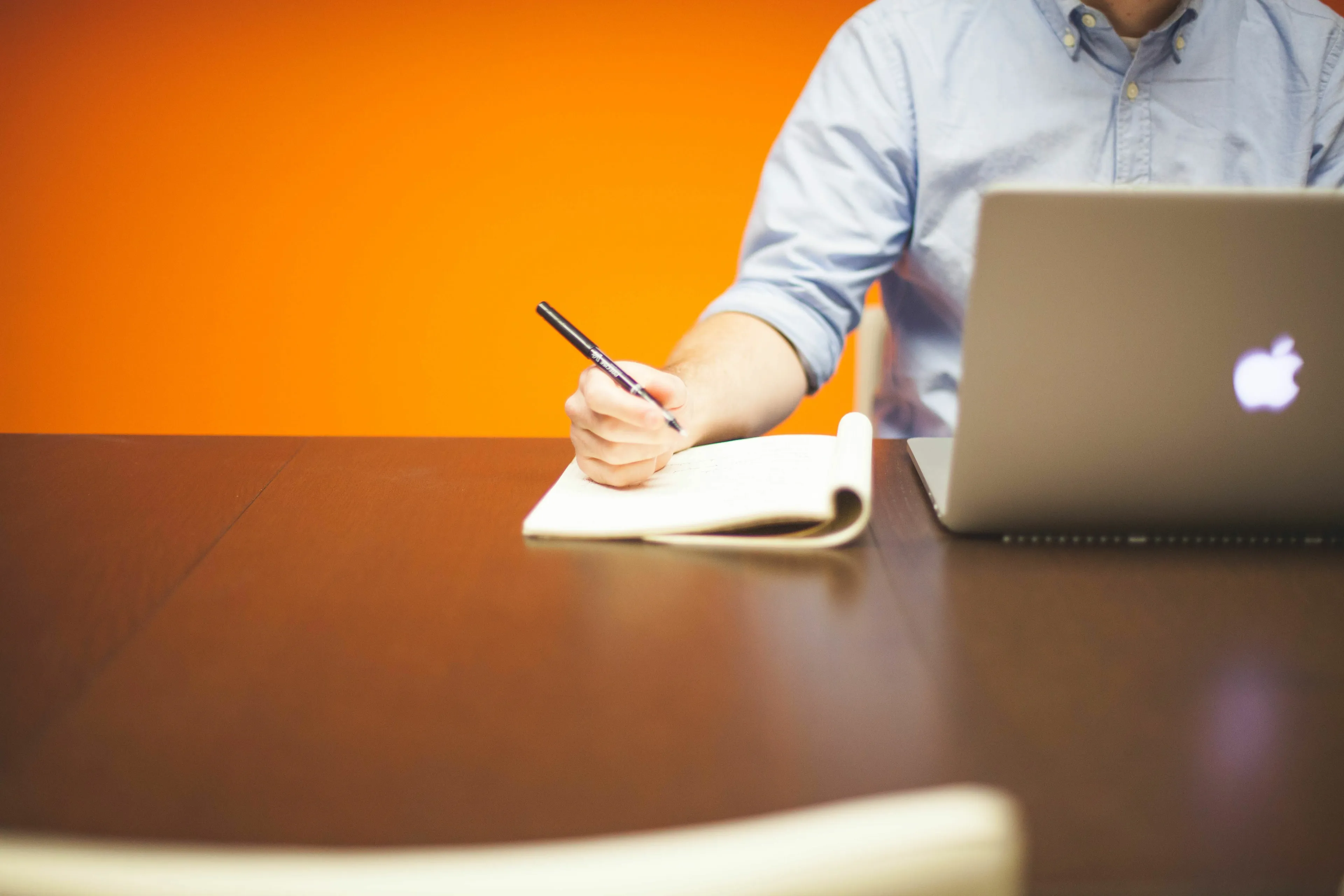 A person in a blue shirt taking notes while using a laptop, representing a work approach for your born decade.