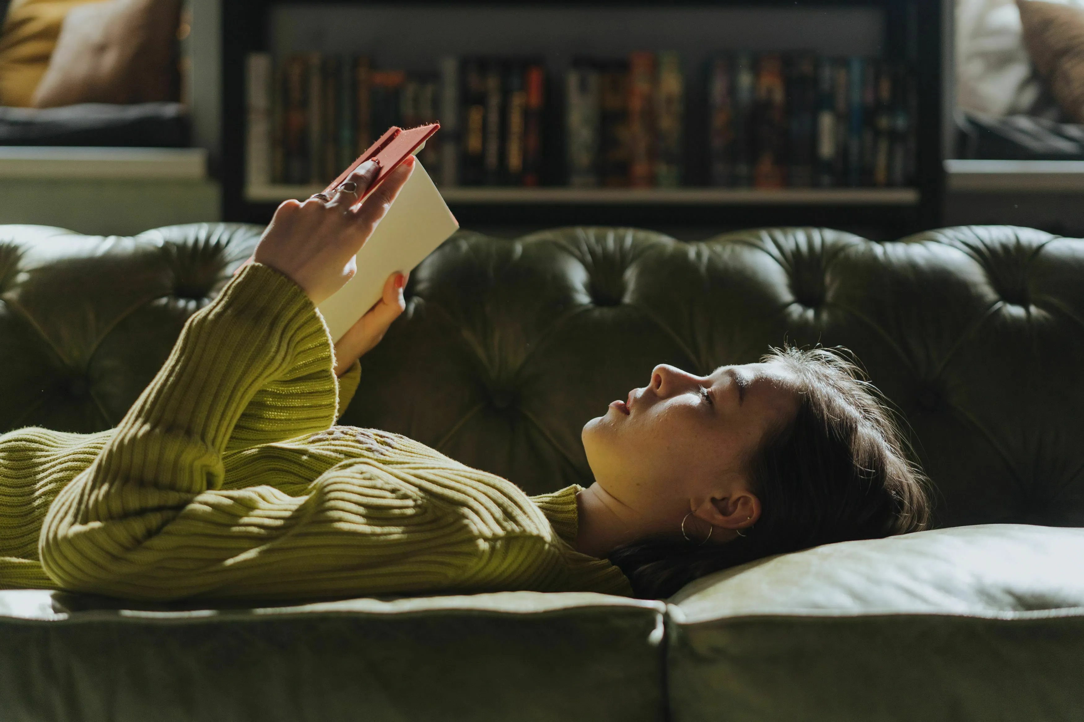 A person reading a book on a green couch, symbolizing what kind of story pulls you in for your born decade.
