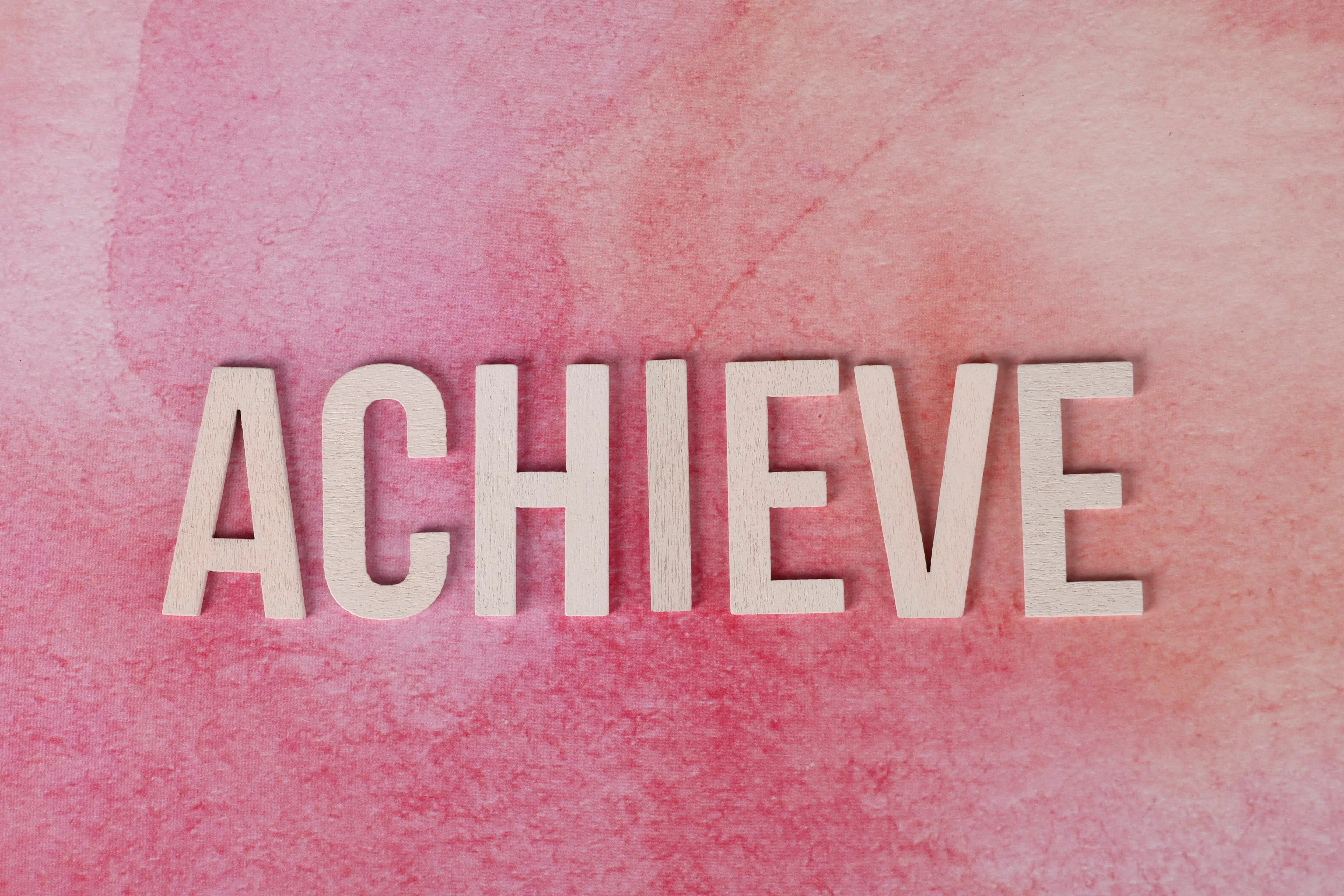 The word ACHIEVE in wooden letters on a pink background, representing ambition for your born decade.
