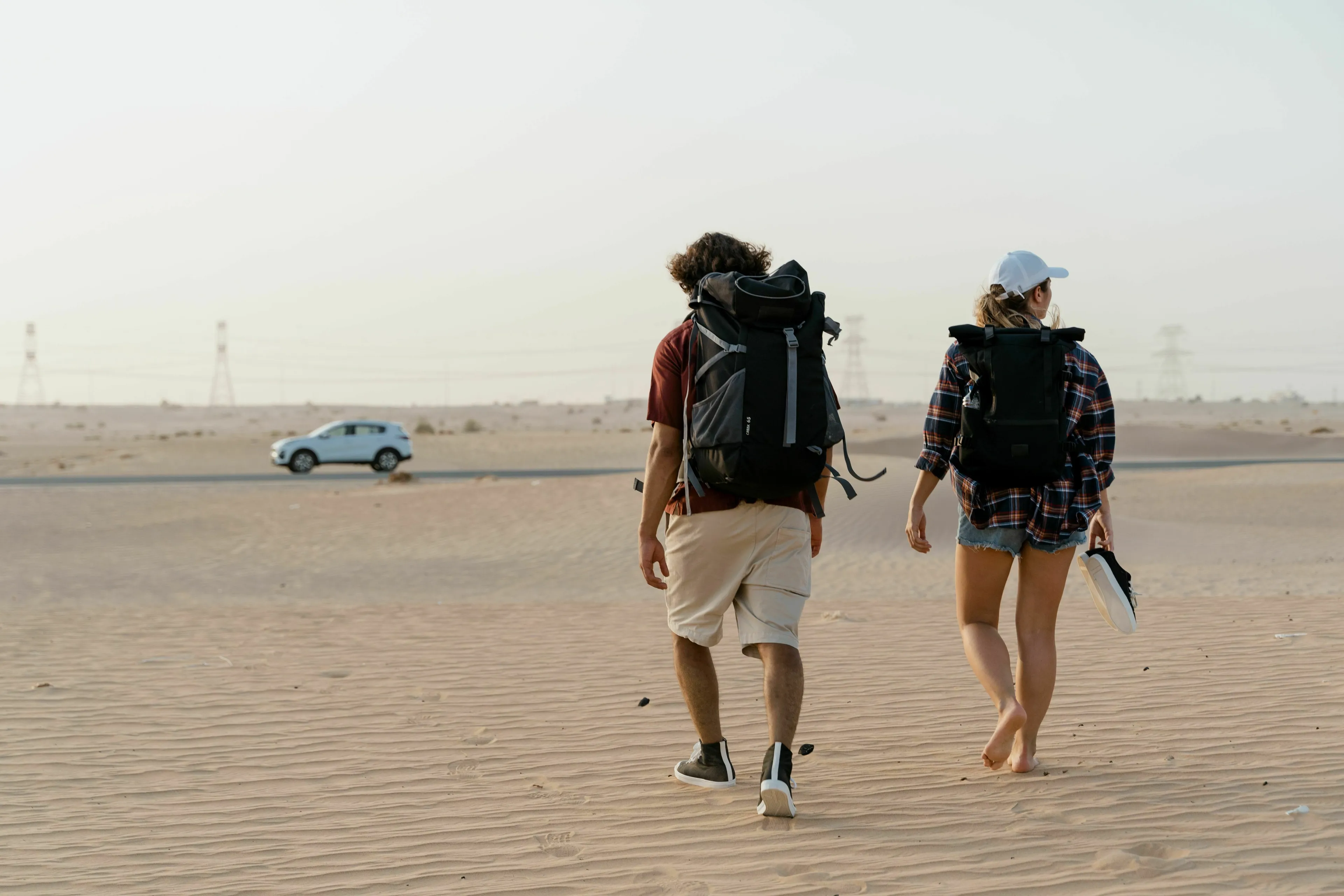 Two hikers with large backpacks walking on a sandy desert road, embodying an ideal mode of travel.