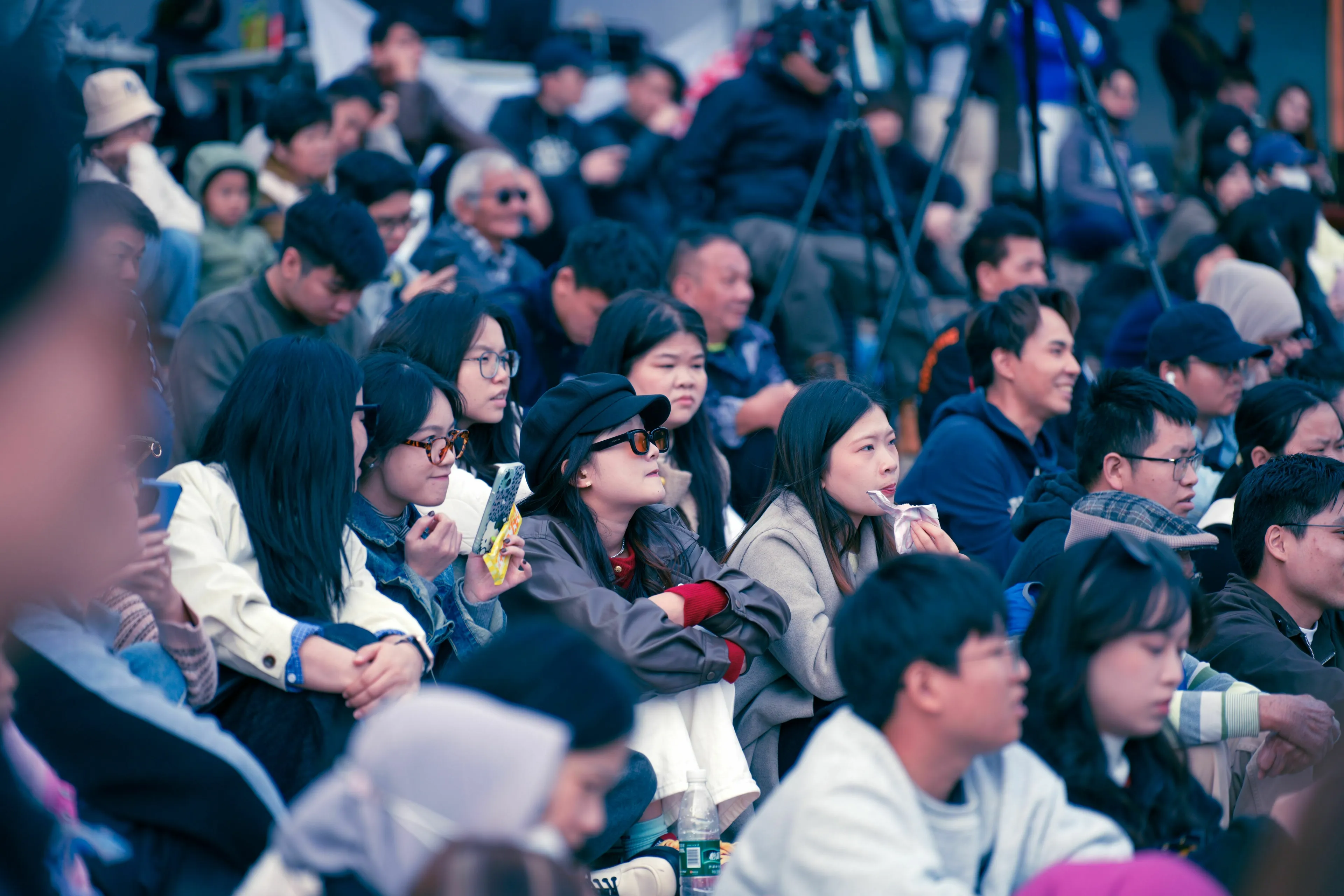 A diverse group of people sitting together outdoors, attentively watching an event, being the center of attention.