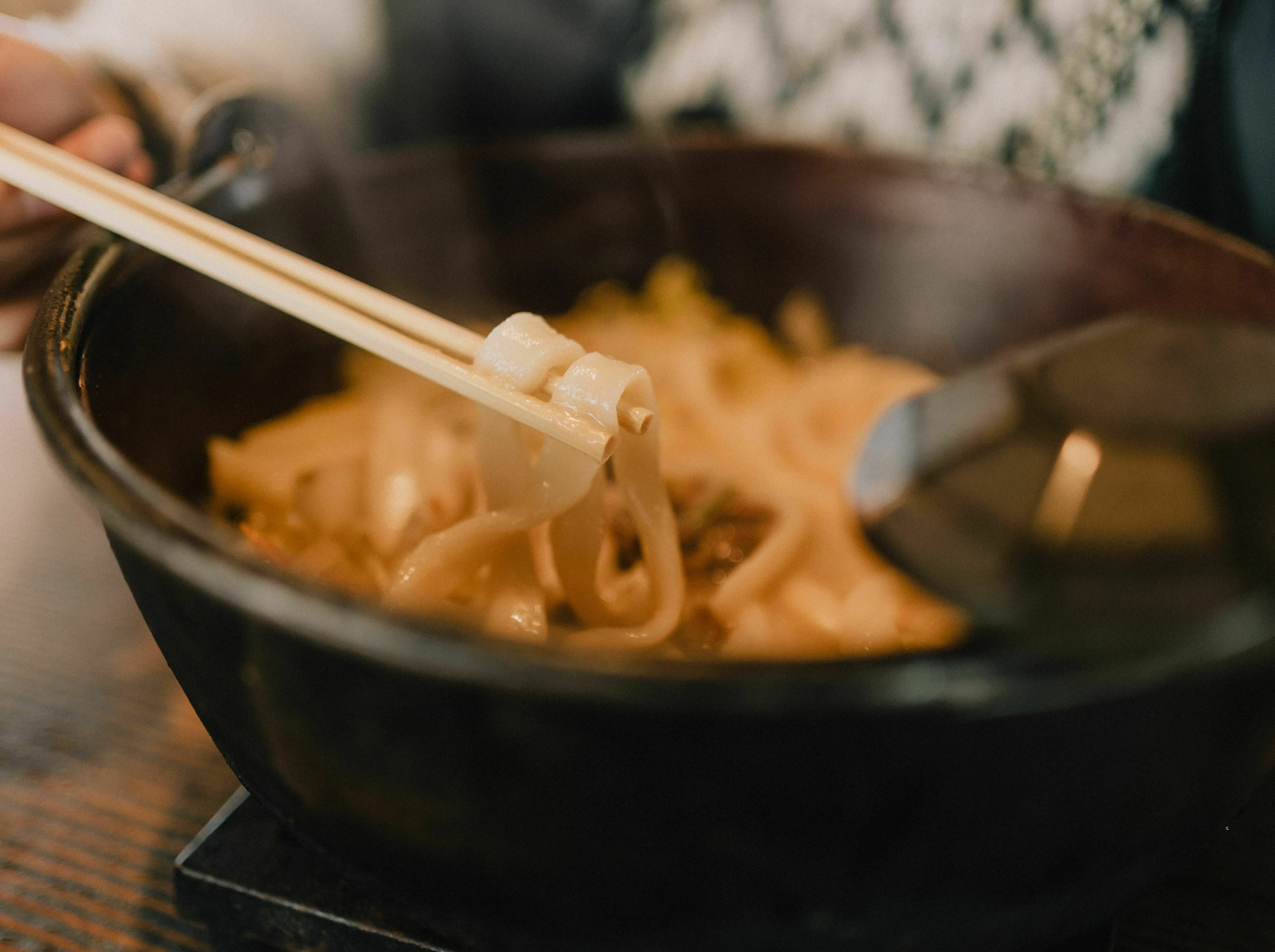 Close-up of chopsticks lifting noodles from a steaming bowl, representing a comforting food scene.