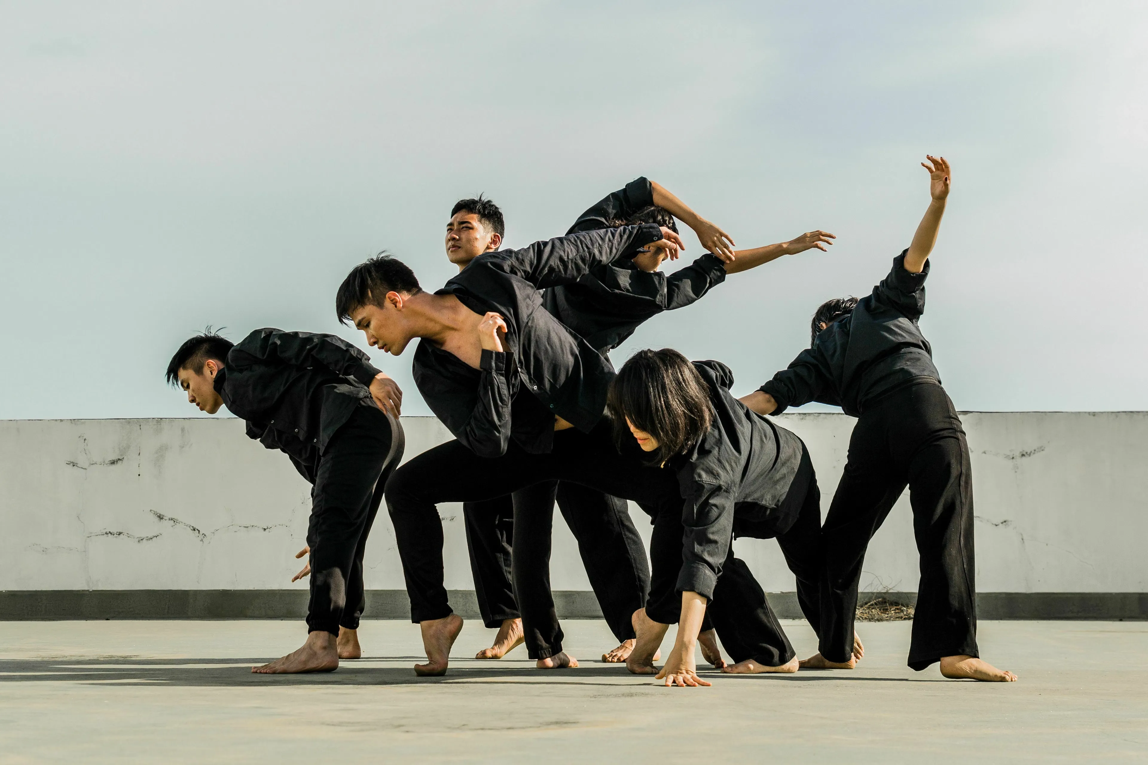 Multiple dancers in black clothing move in unison on a rooftop, showcasing their dancing style.