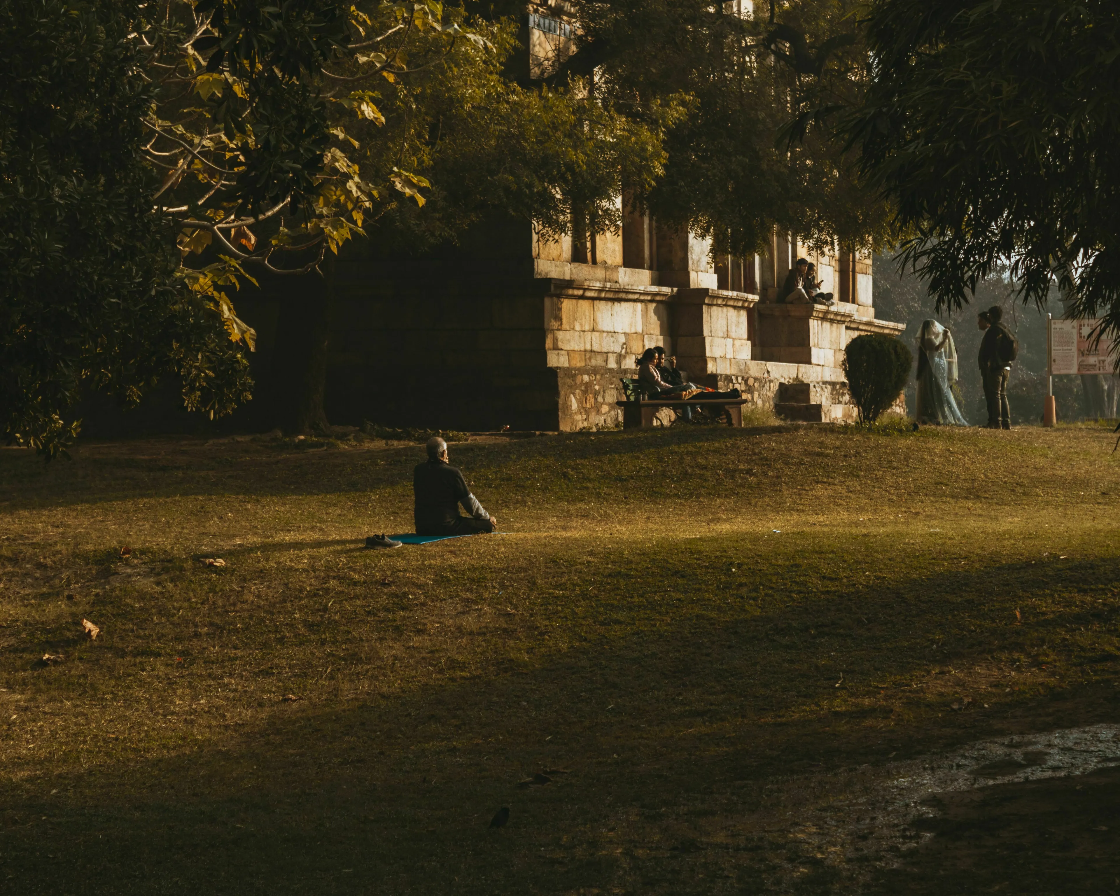 Historical figure sits alone on a mat in a park, enjoying a blank afternoon with no plans.