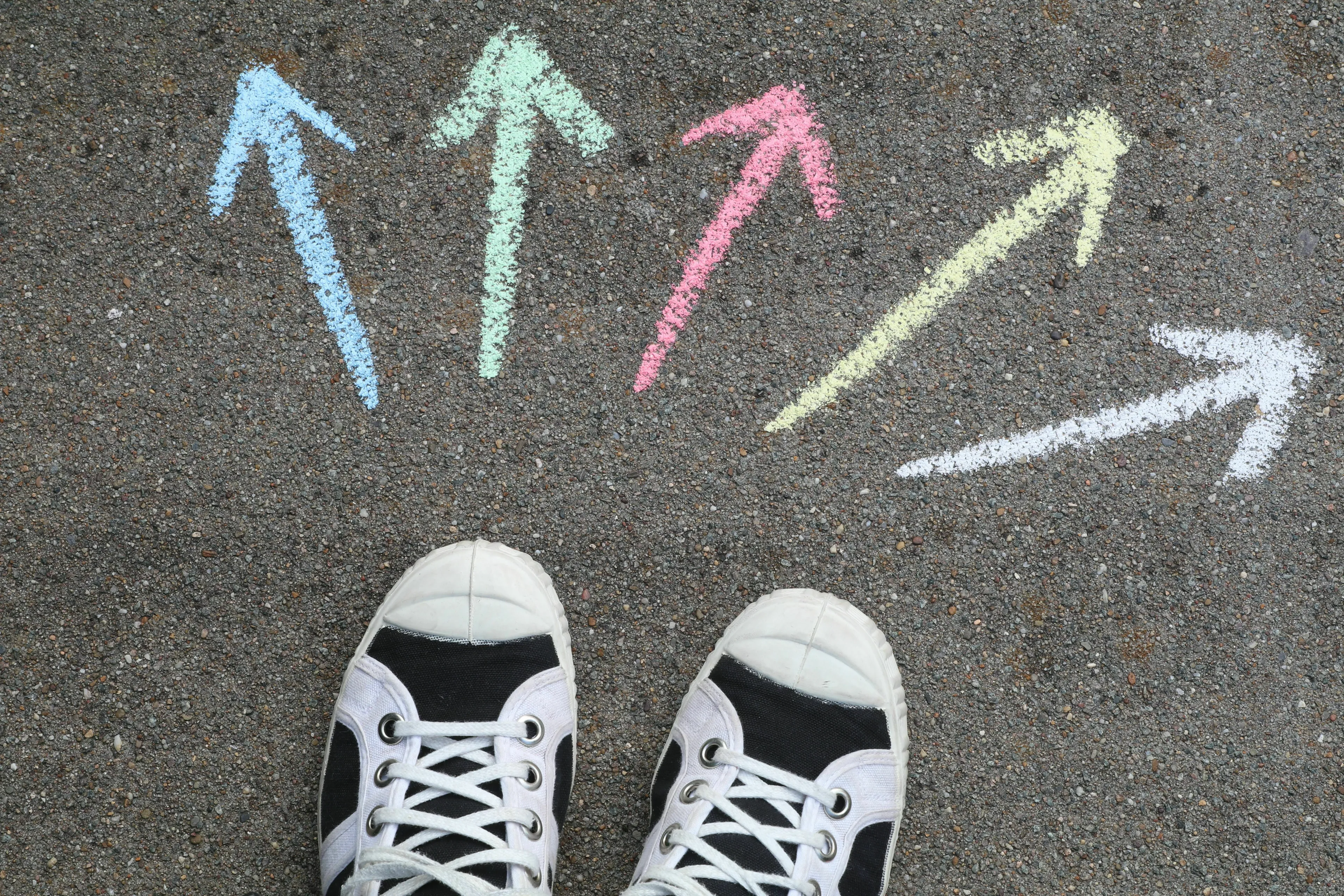A pair of shoes standing on asphalt with chalk arrows pointing in different directions. How do you make a big decision?